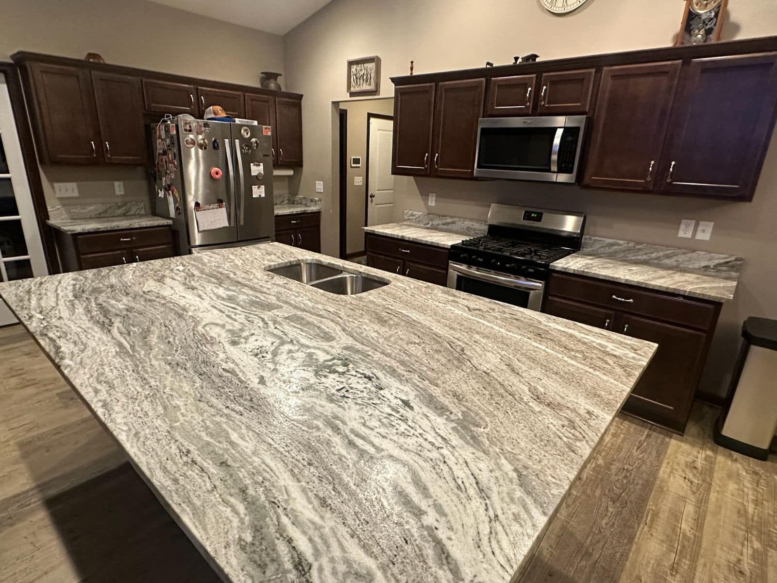 A kitchen with granite counter tops , stainless steel appliances , and brown cabinets.
