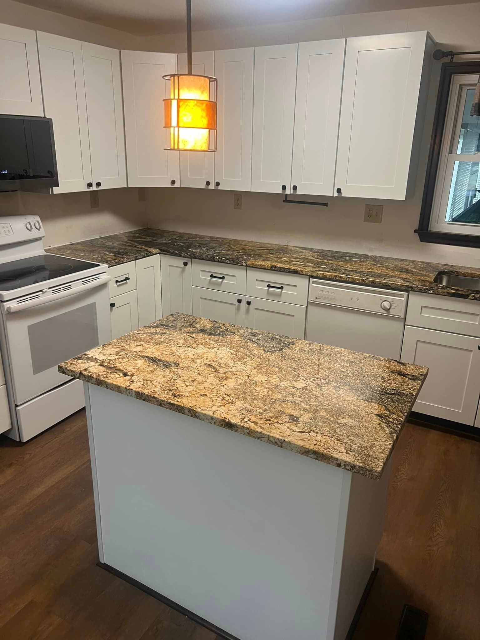 A kitchen with granite counter tops , white cabinets , a stove , and a large island.