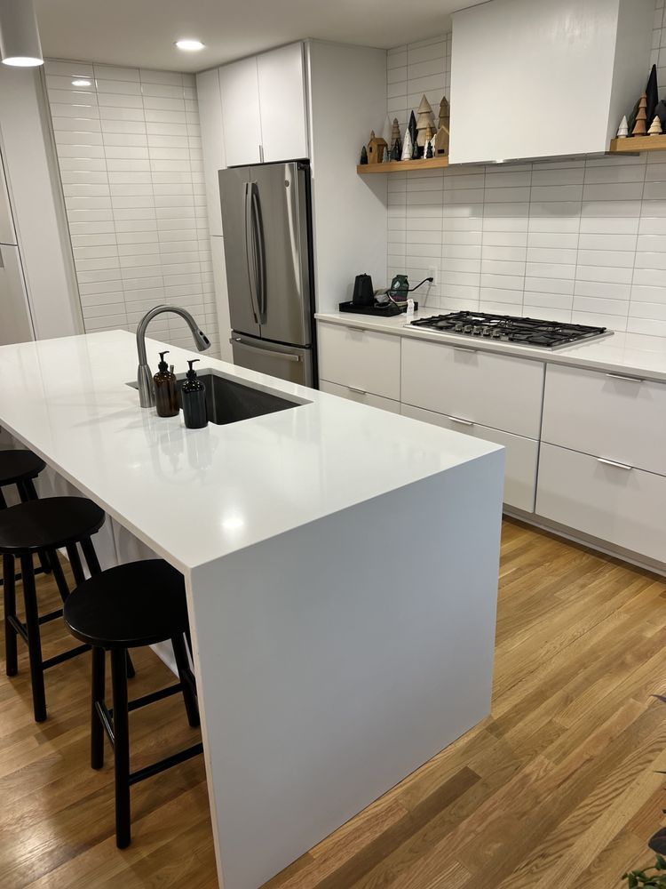 A kitchen with white cabinets , a large island , a sink , a refrigerator , and a stove.