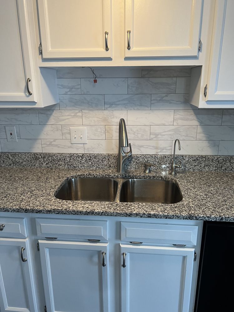 A kitchen sink with granite counter tops and white cabinets.