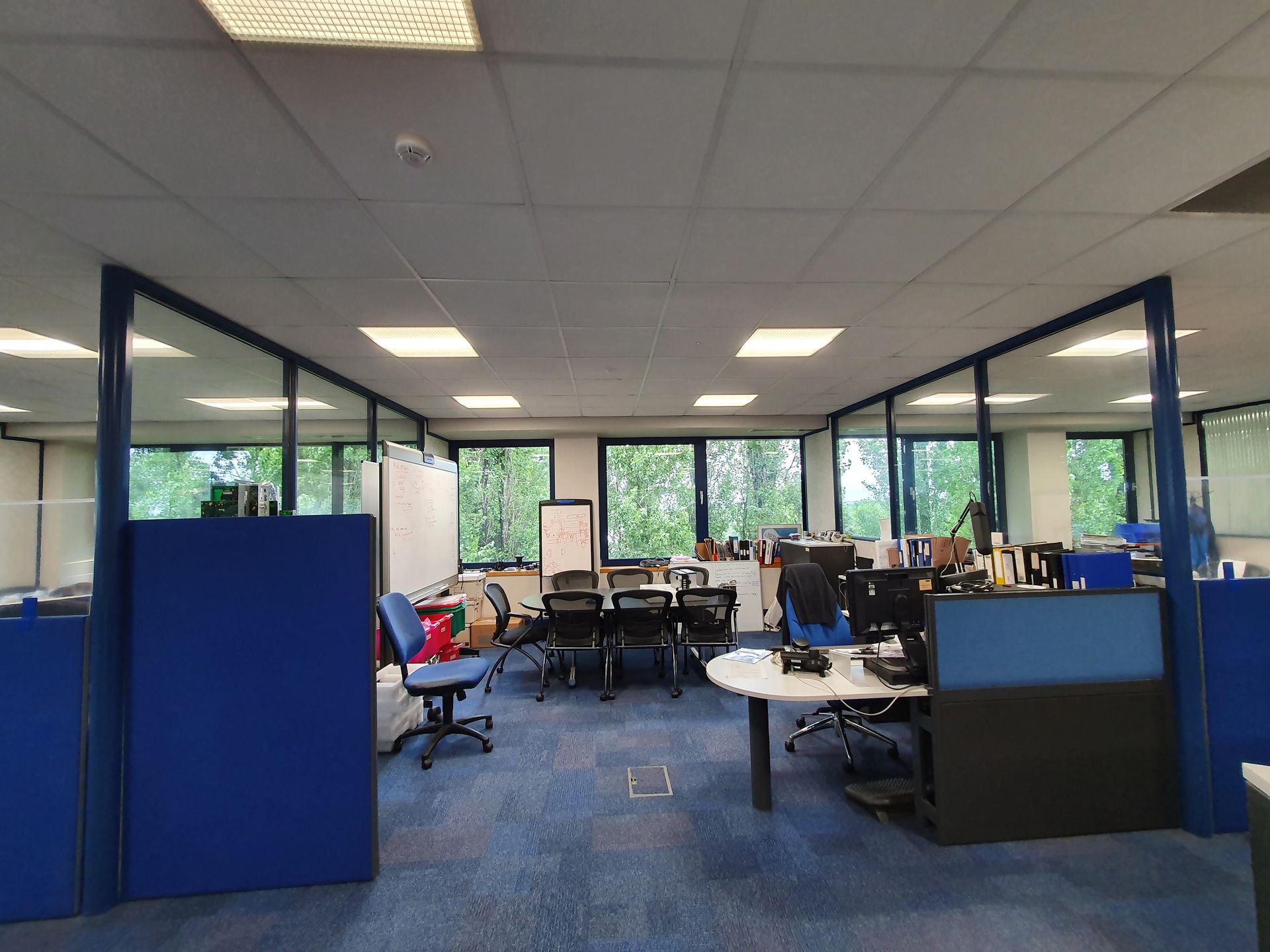 A desk and meeting table in a dated office with blue partitioning.