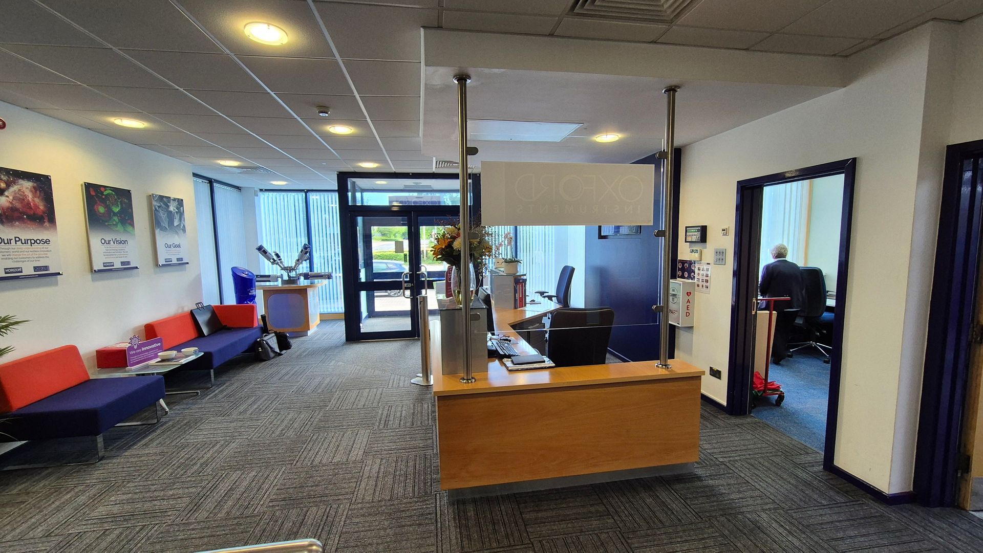 A dated office reception area with a wooden desk and glass partition