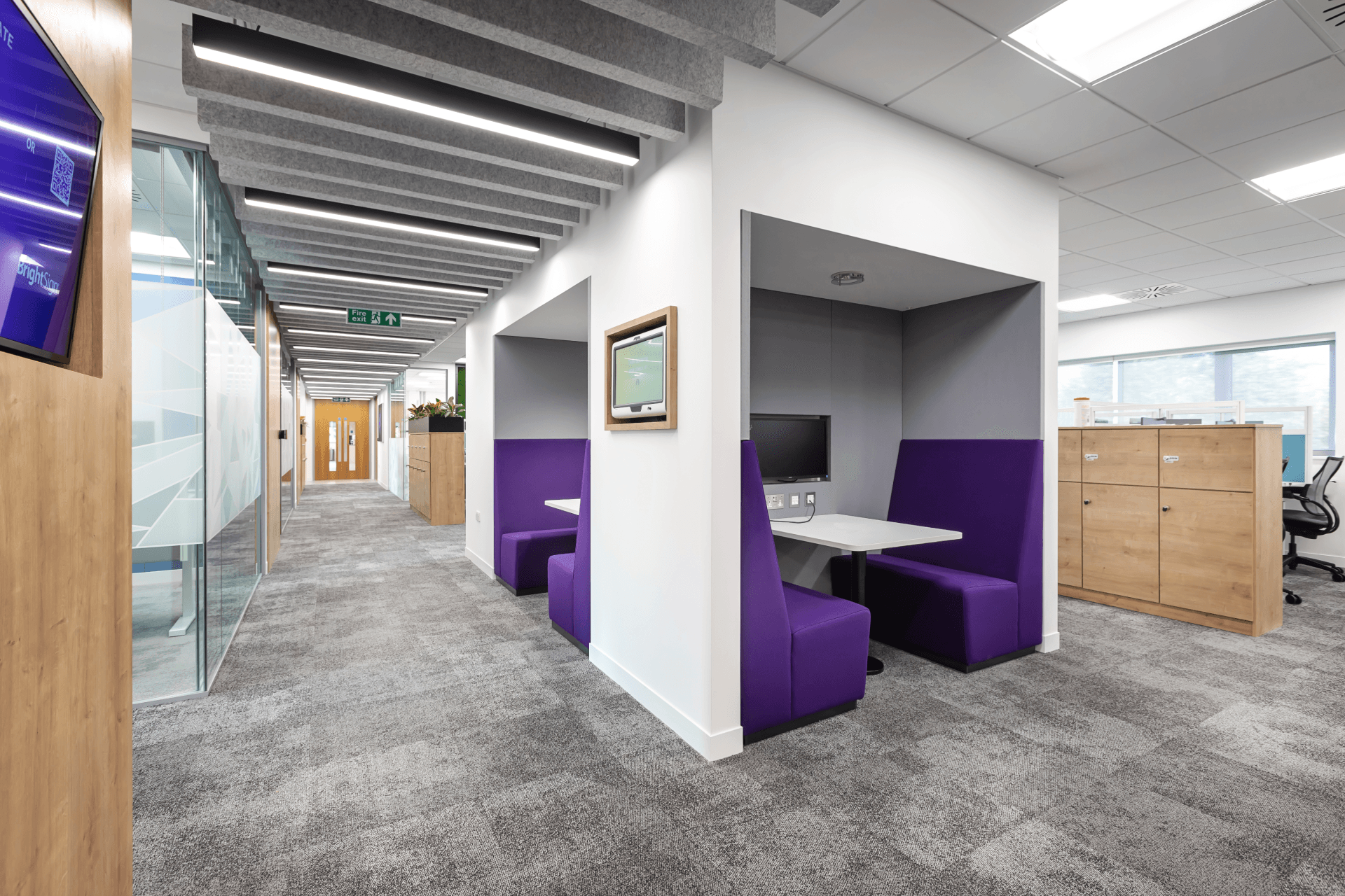 a hallway in an office with purple booths and a table .