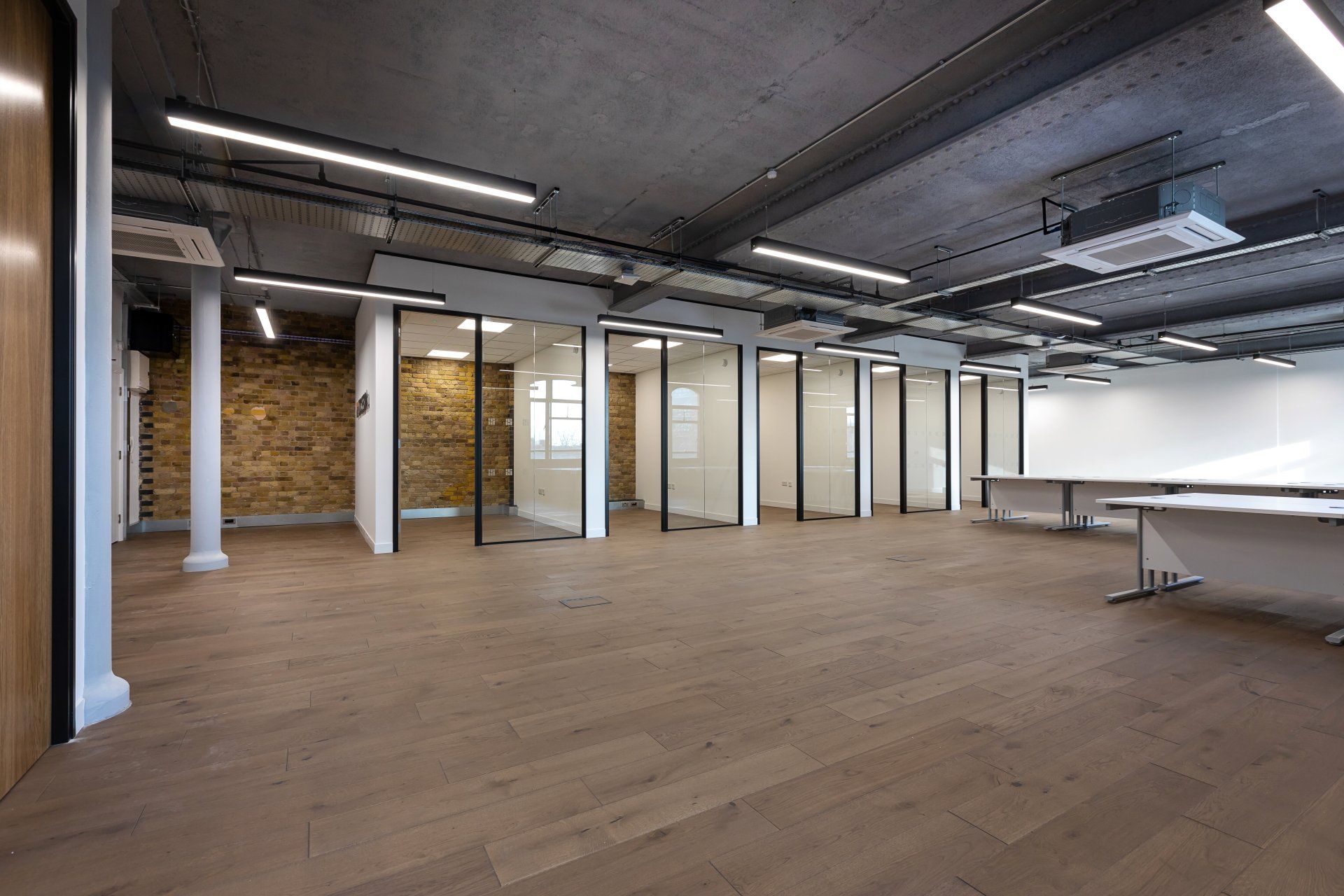 A large empty office space with wooden floors and glass partitions.