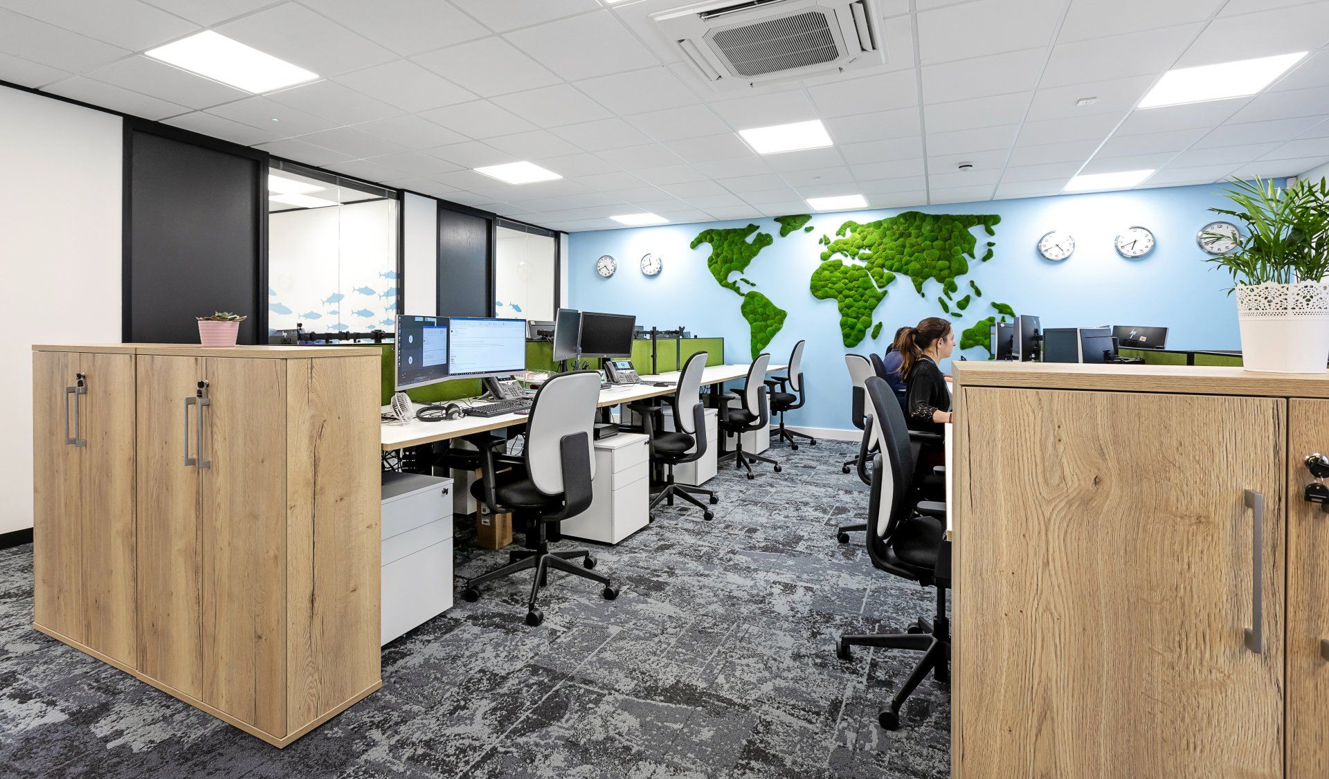 A woman is sitting at a desk in an office with a map of the world on the wall.