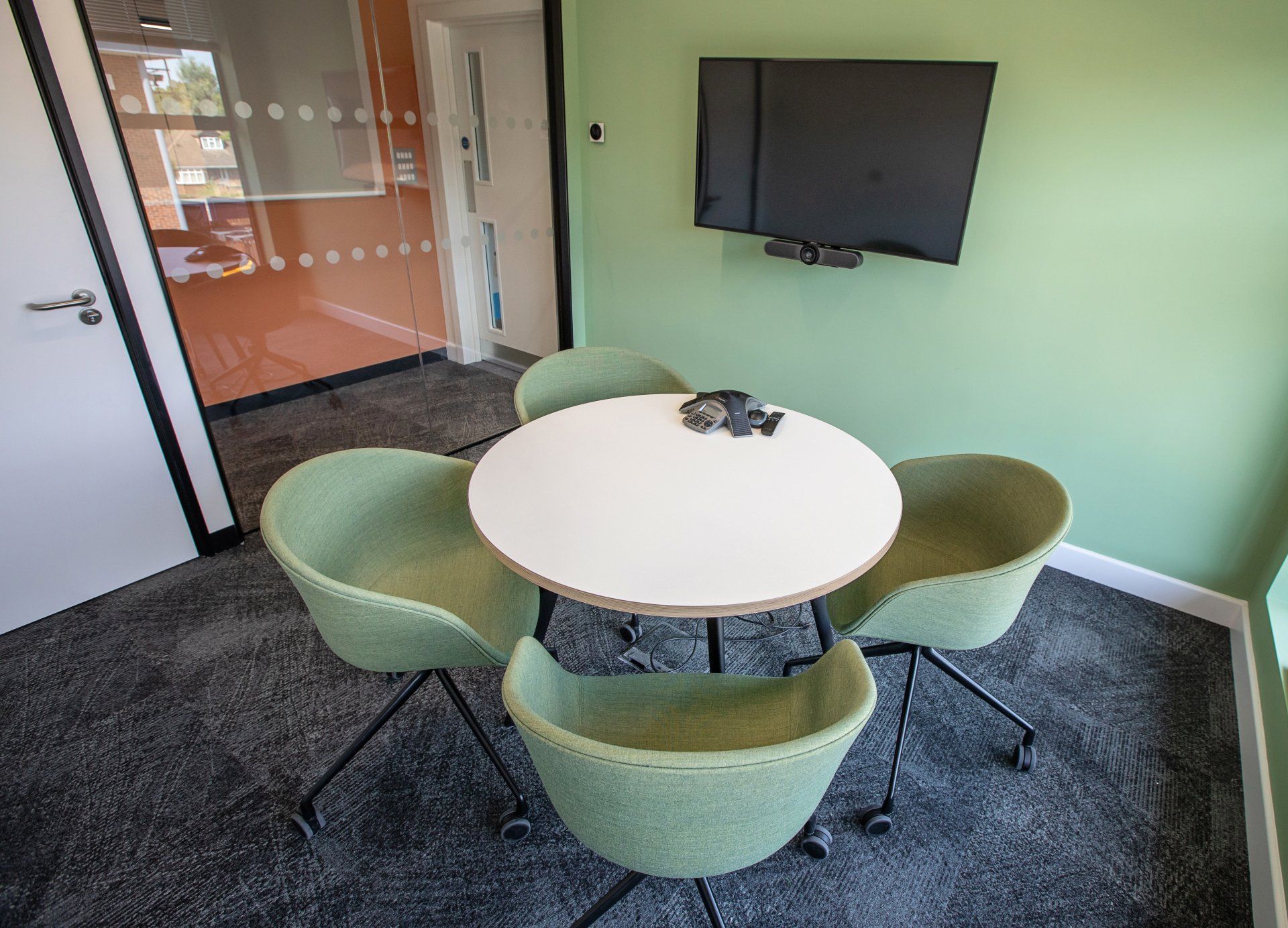 A conference room with a round table and chairs and a flat screen tv.