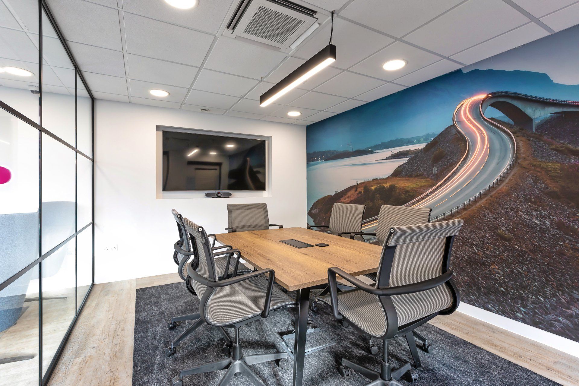 A conference room with a table and chairs and a picture of a road on the wall.