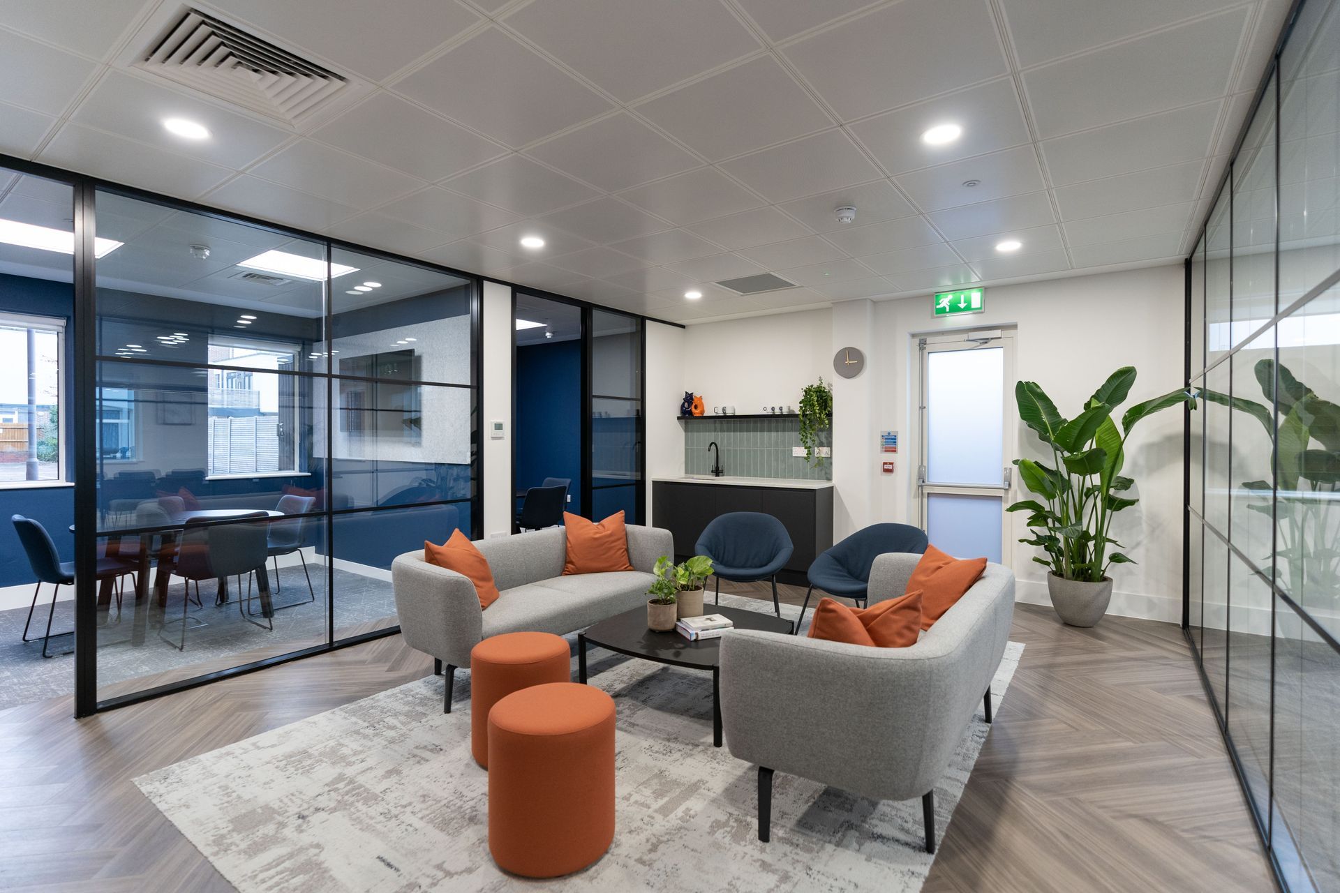 A modern office space room with a grey sofa, chairs ,ottomans and a table.
