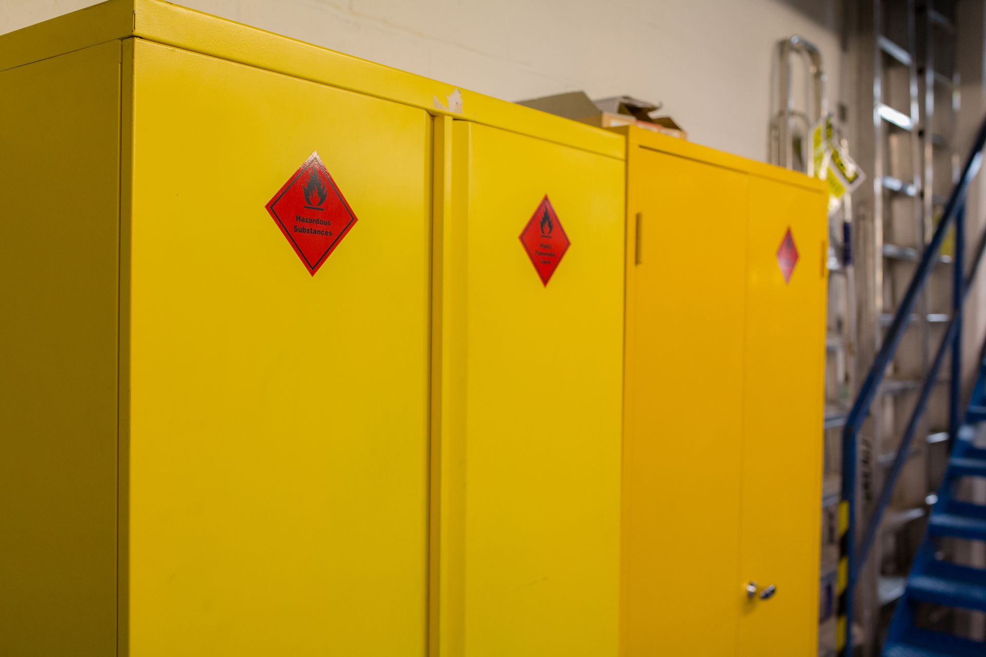 A row of yellow flammable cabinets in a room next to stairs.