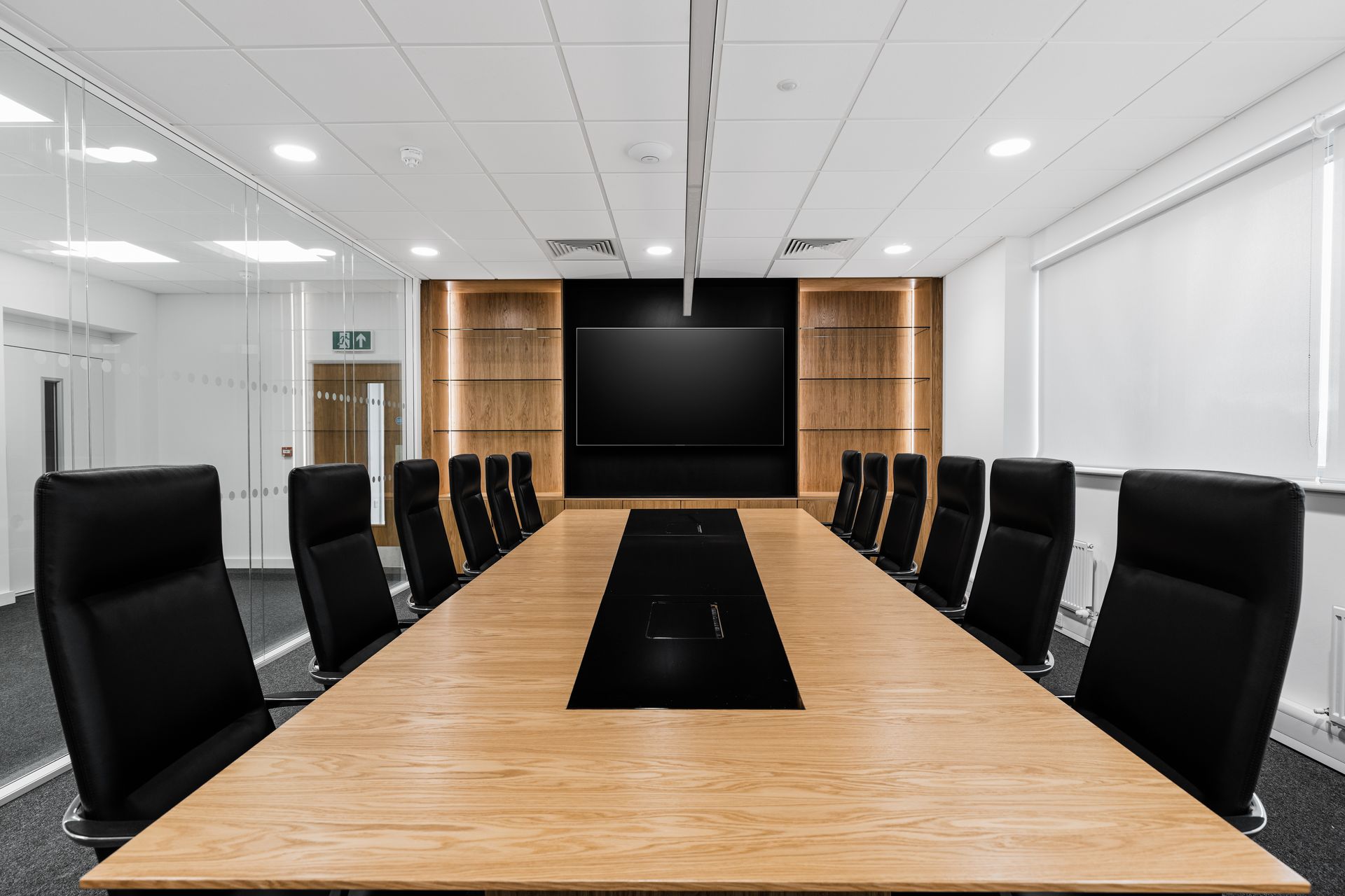 A conference room with a long wooden table and black chairs.