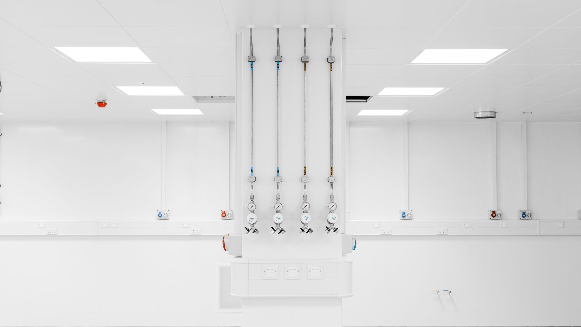 A white room with a lot of pipes hanging from the ceiling.
