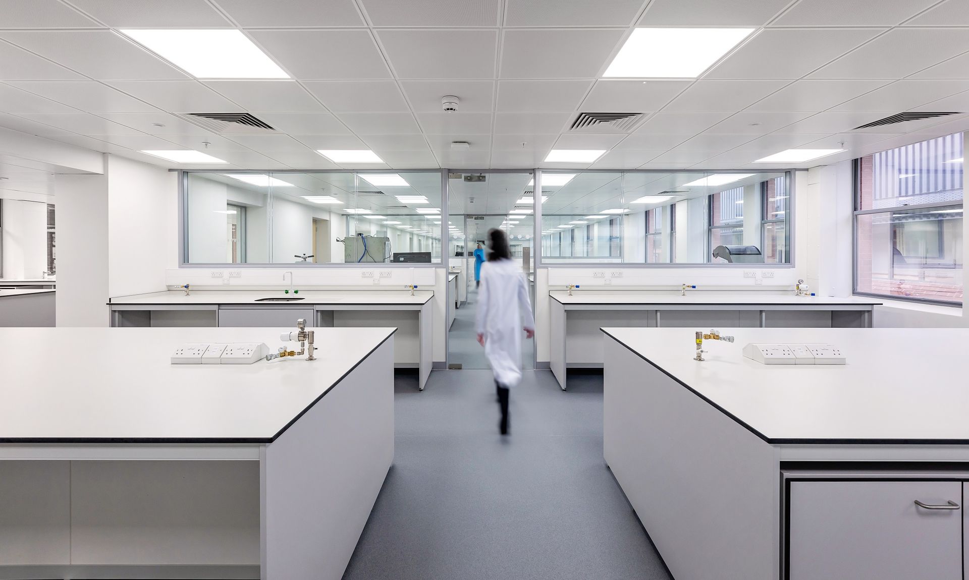 a woman in a lab coat is walking down a hallway in a laboratory .