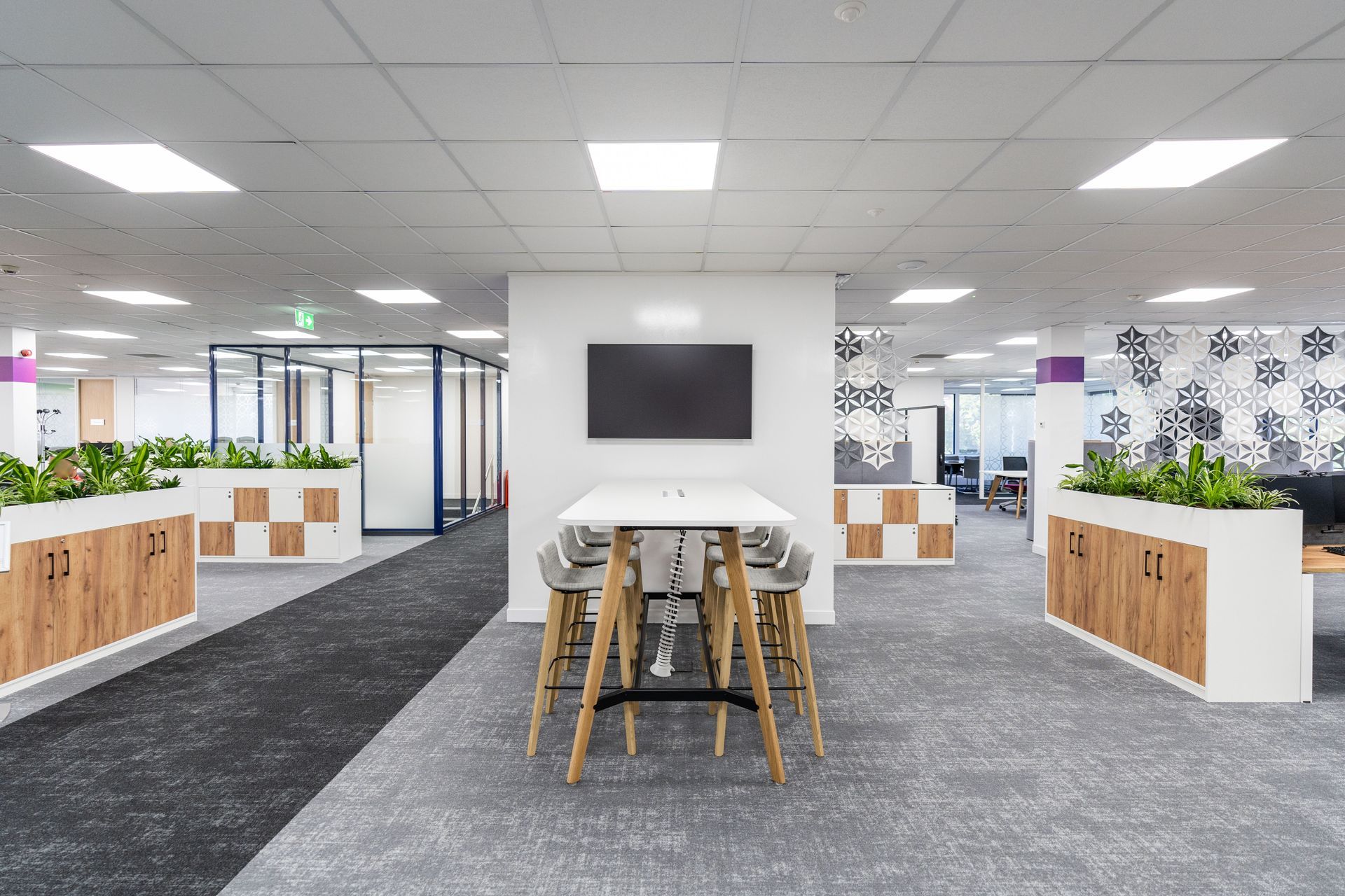 Modern office interior with desks, plants, and a central table with chairs.