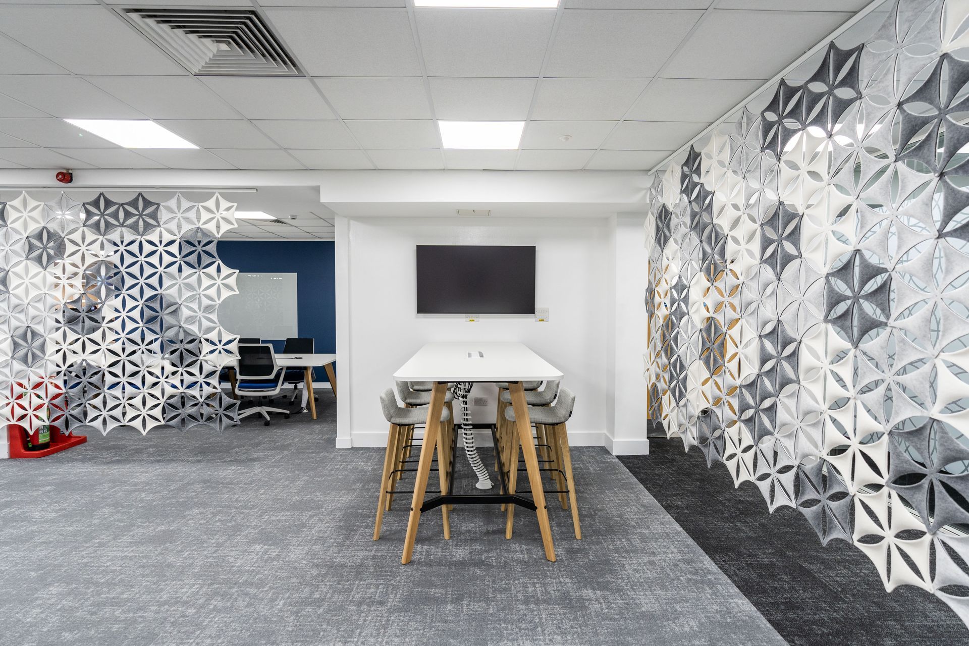 A meeting table in a modern, bright office with grey and white partitioning and a screen on the wall.