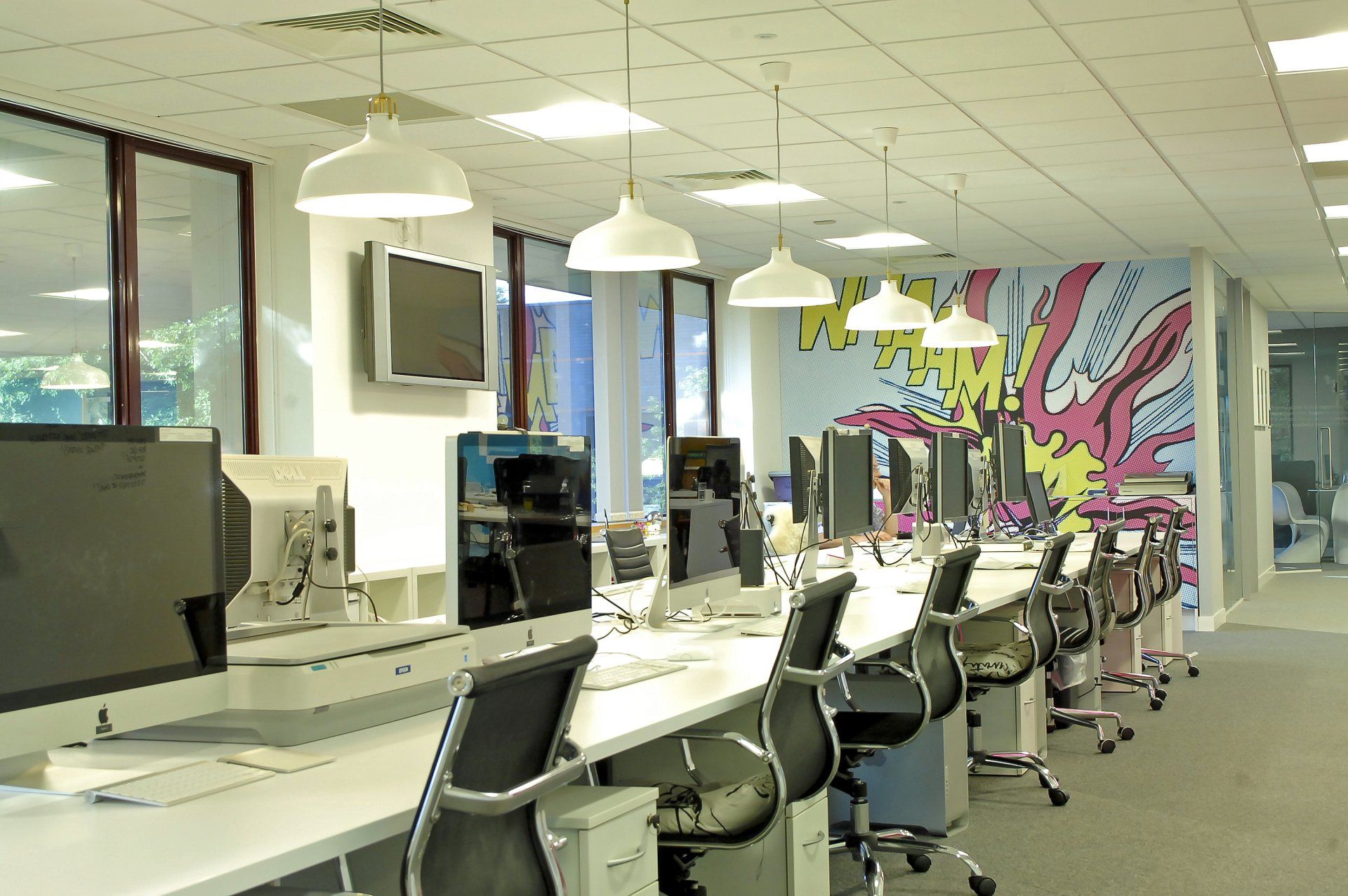 A row of desks and chairs in an office with a mural on the wall