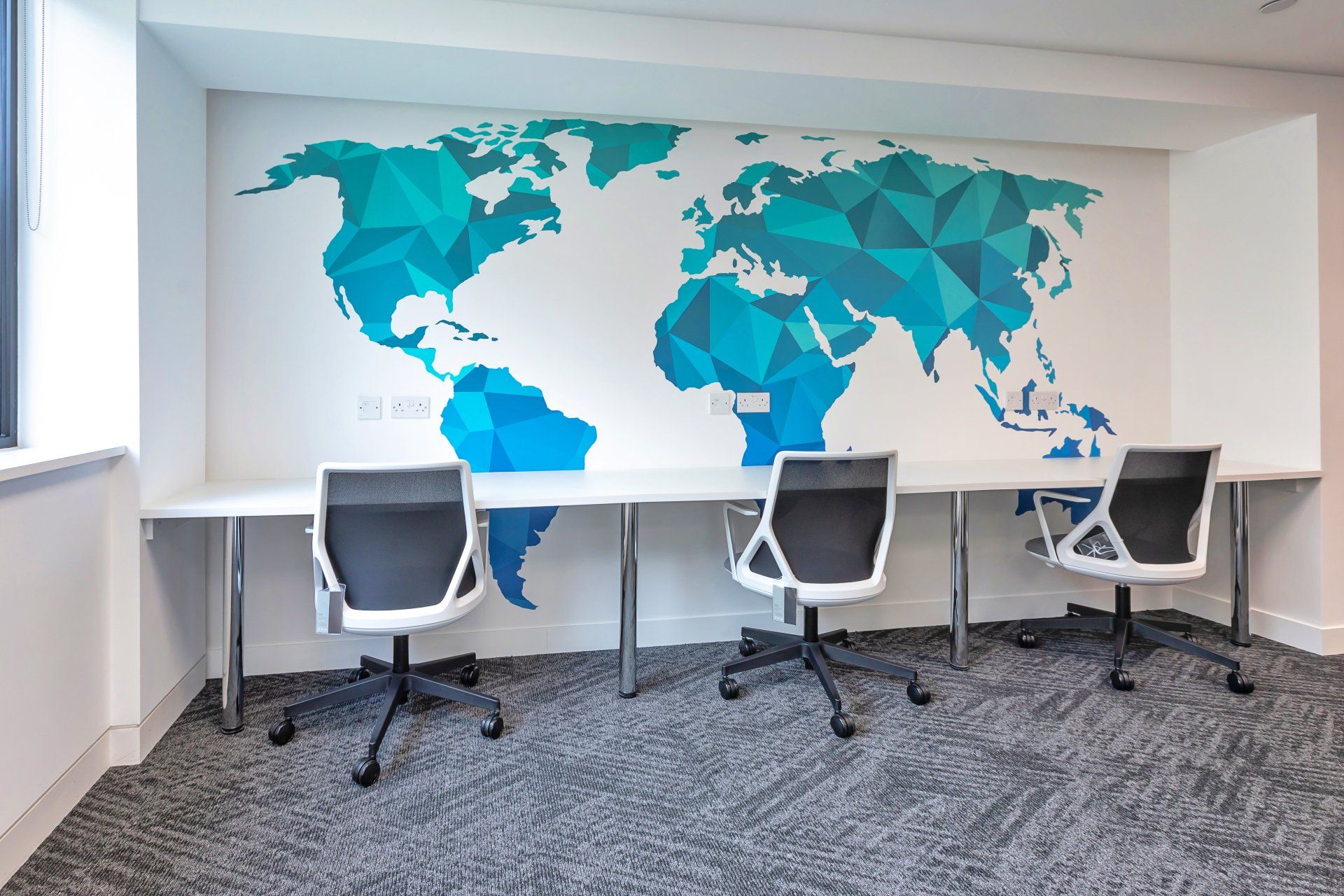 A room with three desks and chairs and a map of the world on the wall.