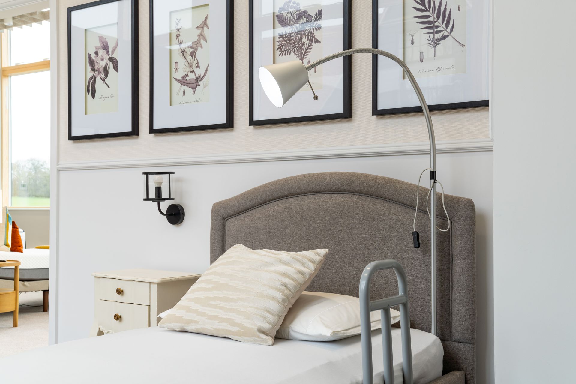 A bedroom with a bed, nightstand, lamp, and paintings on the wall.