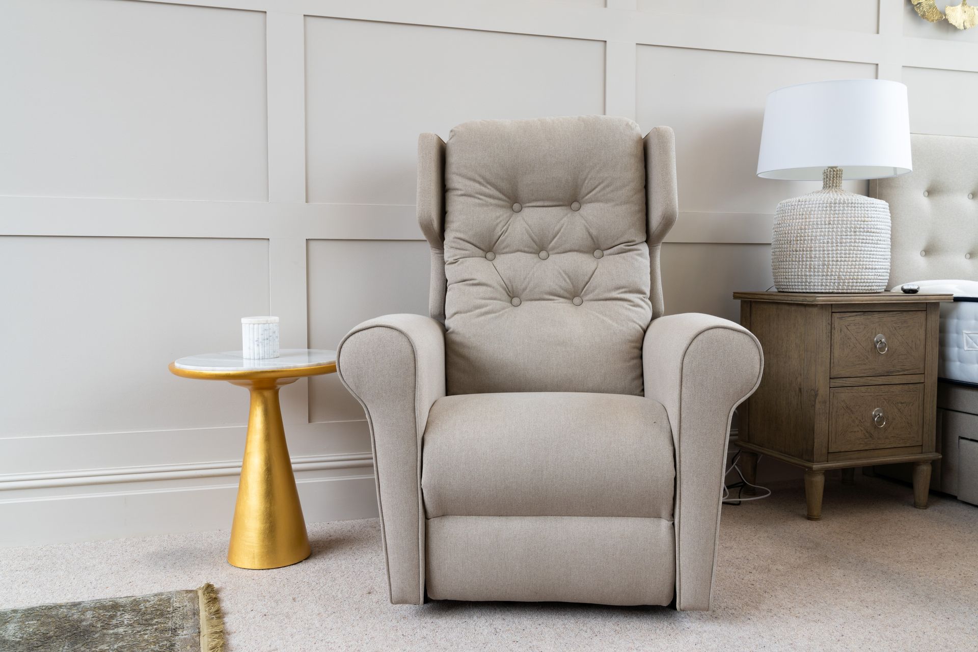 A recliner is sitting in a bedroom next to a nightstand and a lamp.