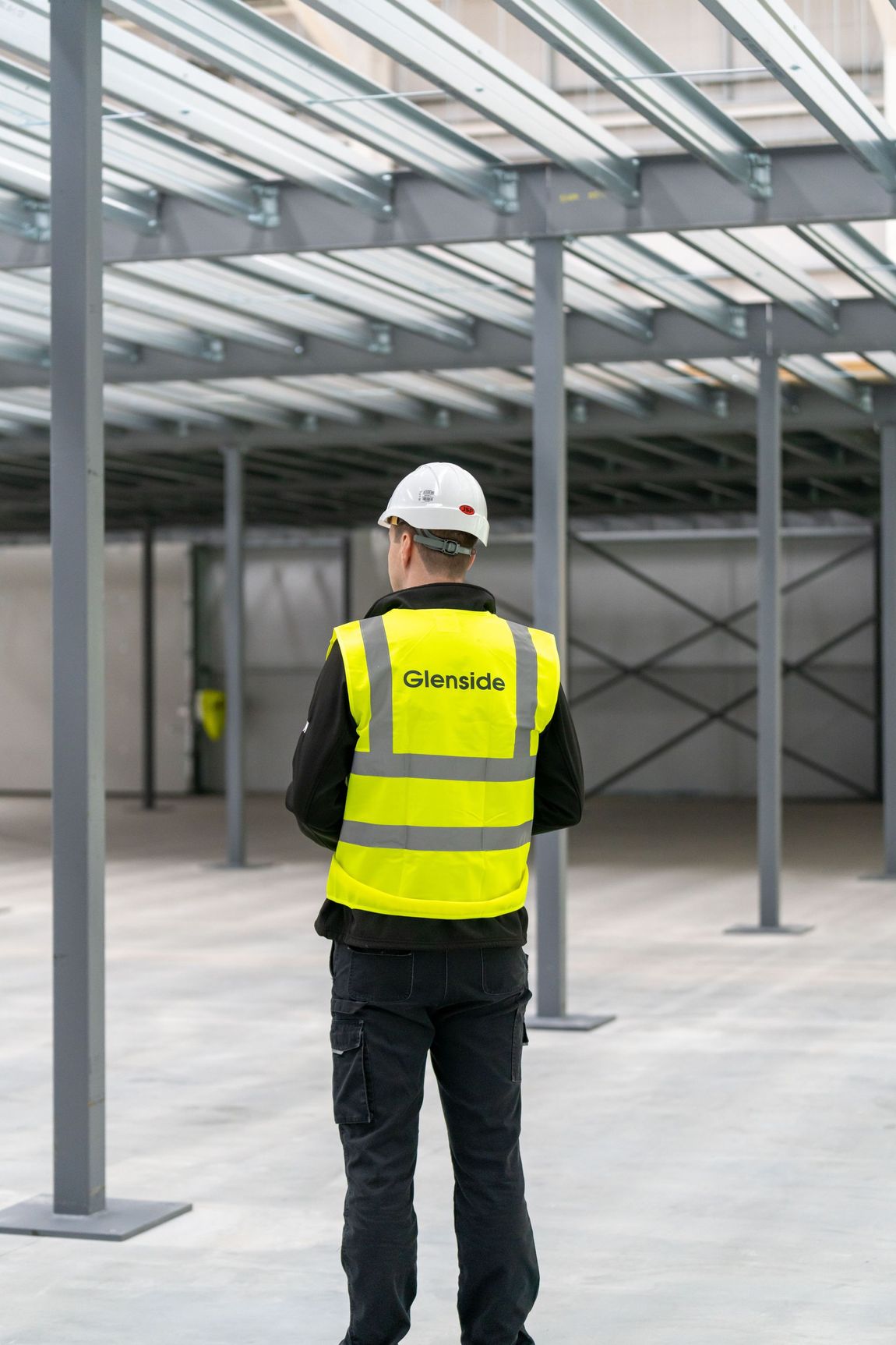 A man wearing a hard hat and a yellow vest is standing in an empty room.
