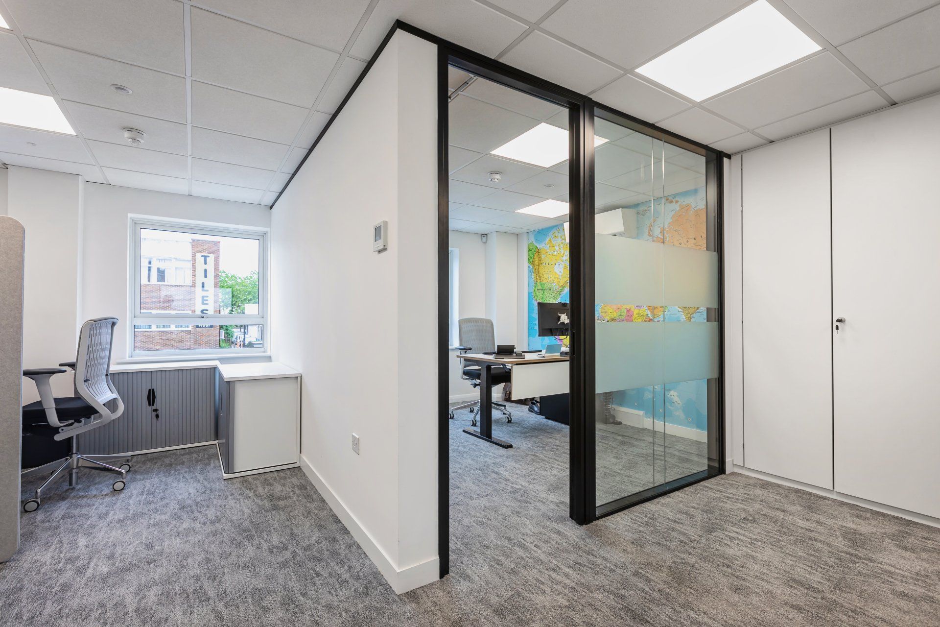 A room with a glass wall and a desk and chairs in it.