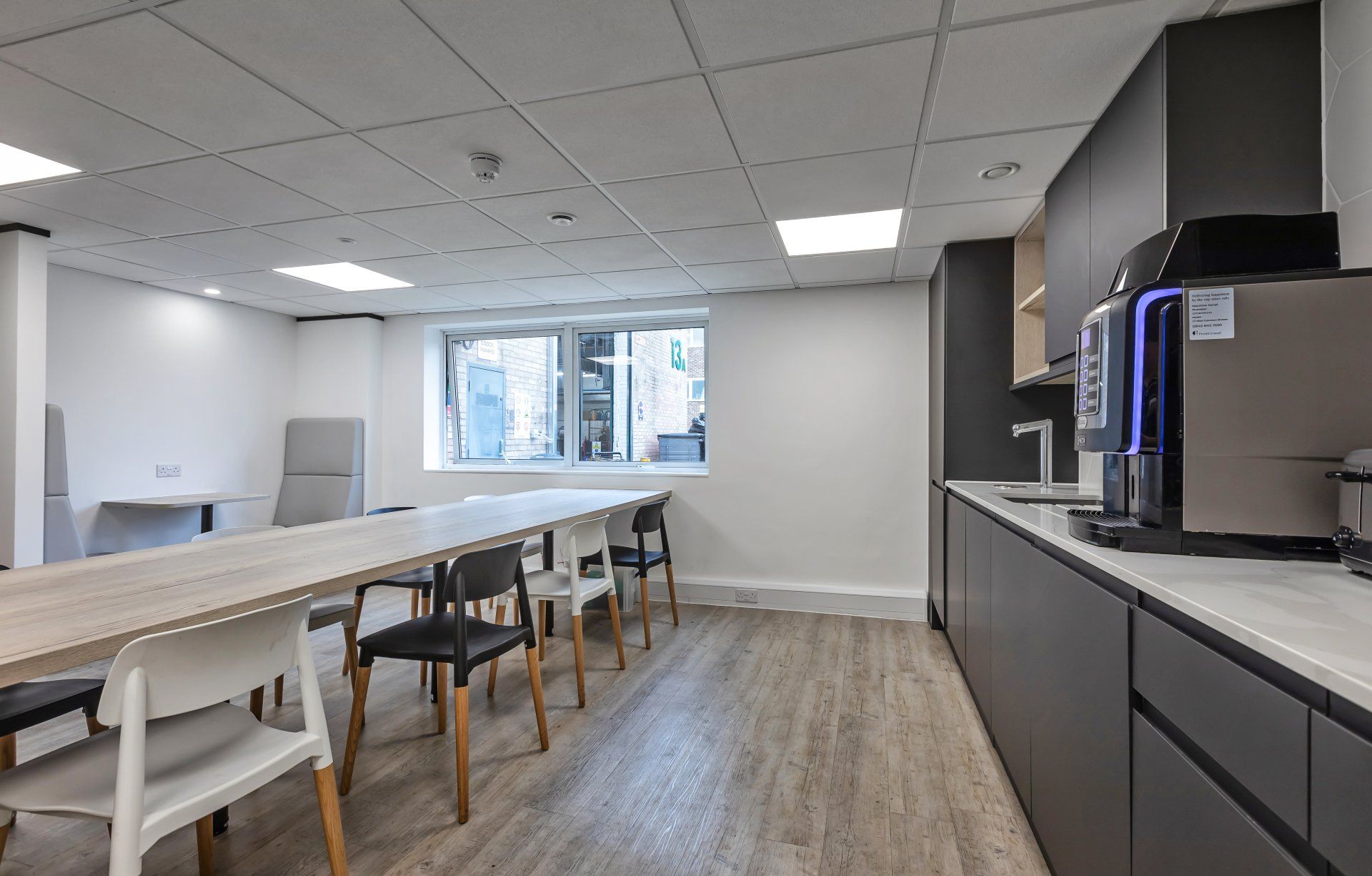 A kitchen with a long table and chairs and a coffee machine.