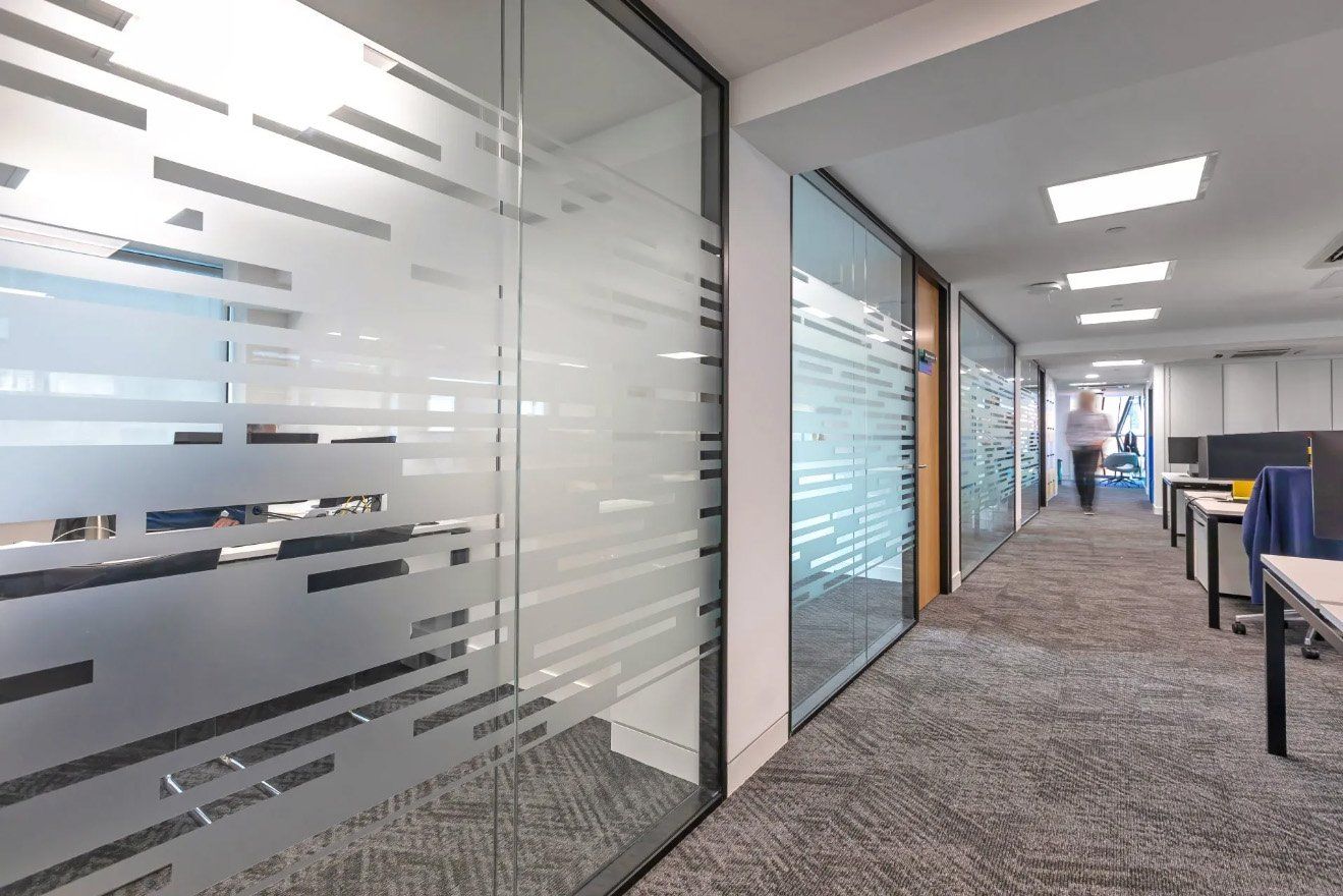 A man is walking down a hallway in an office with a glass wall.