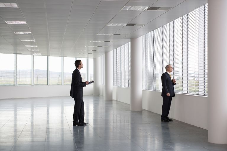 Two men are standing in an empty office looking out the windows