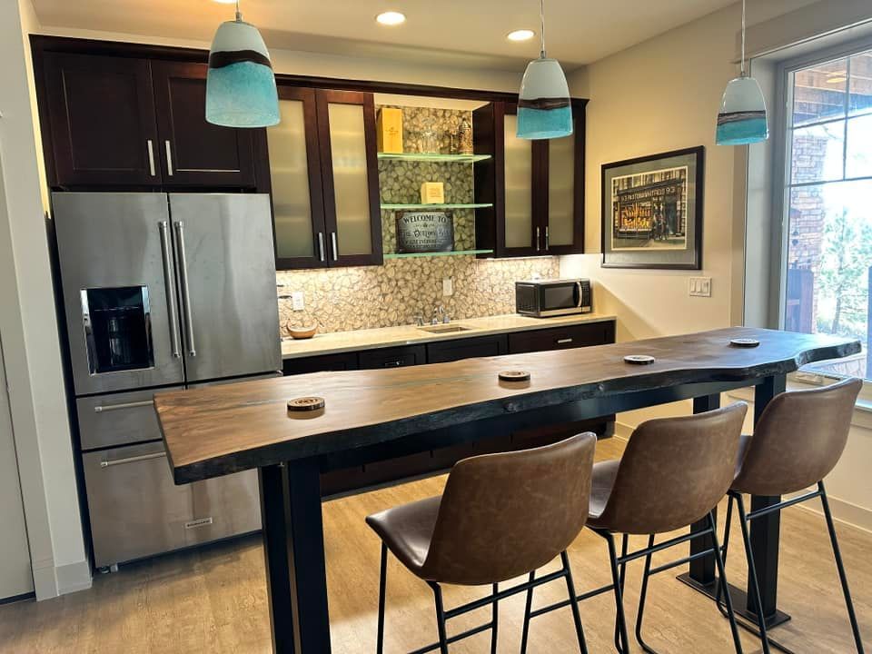 Modern kitchen with dark cabinets, stainless steel refrigerator, patterned backsplash, and wooden bar with three stools.