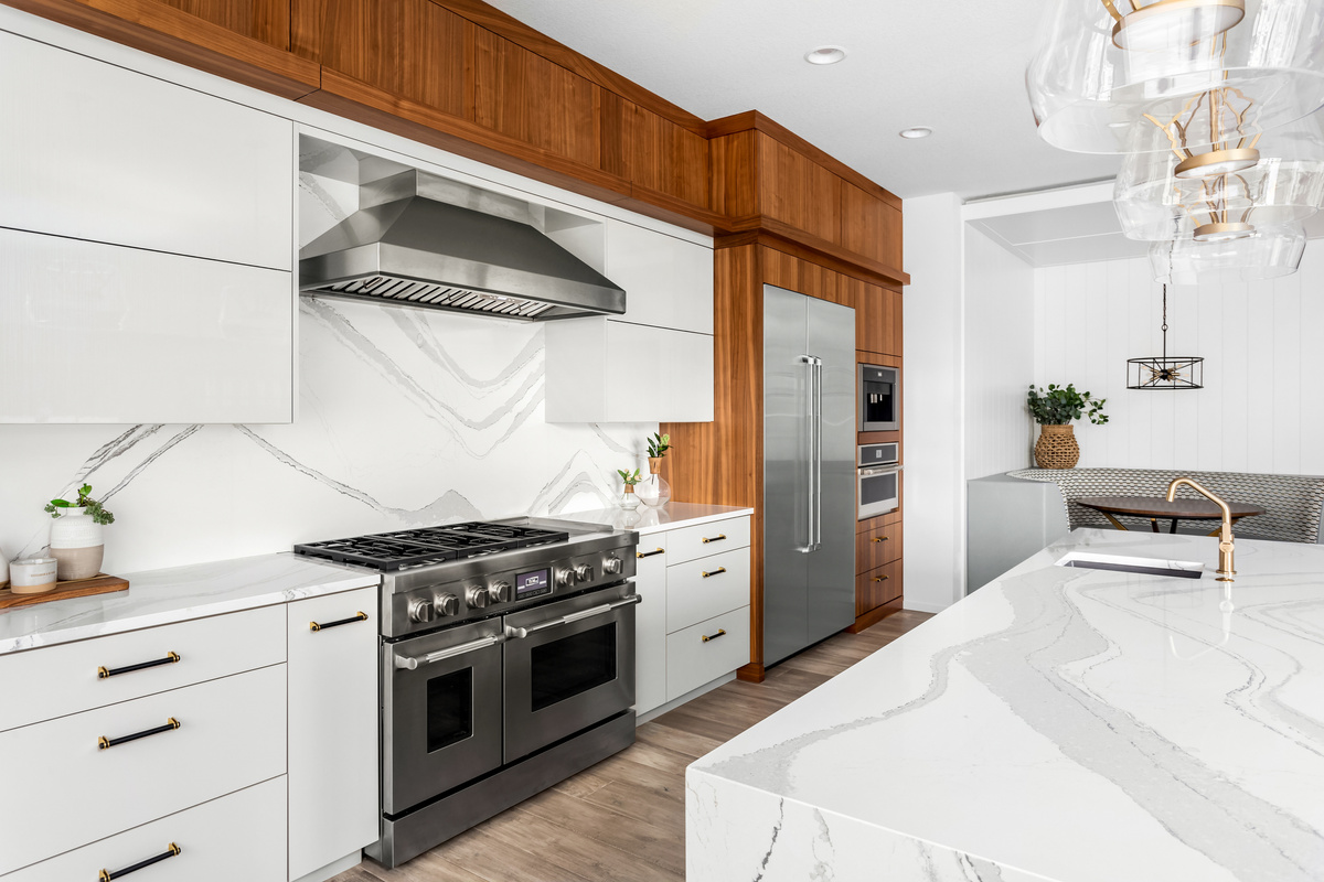 A modern kitchen with white cabinets, marble countertops, stainless steel appliances, and wood-toned upper cabinetry.