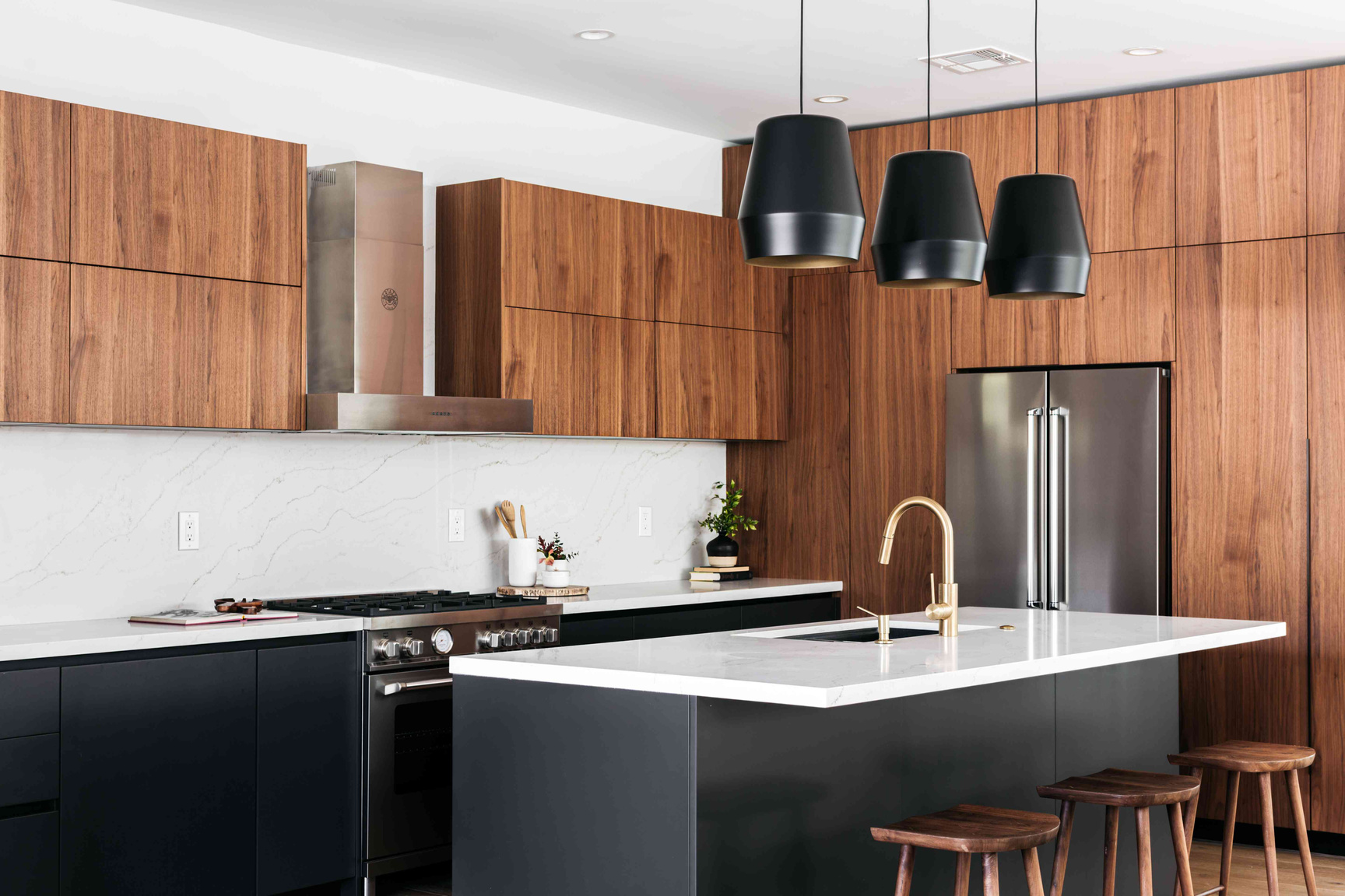 A modern kitchen with wood-toned upper cabinets, a black base, white countertops, stainless steel appliances, and island.