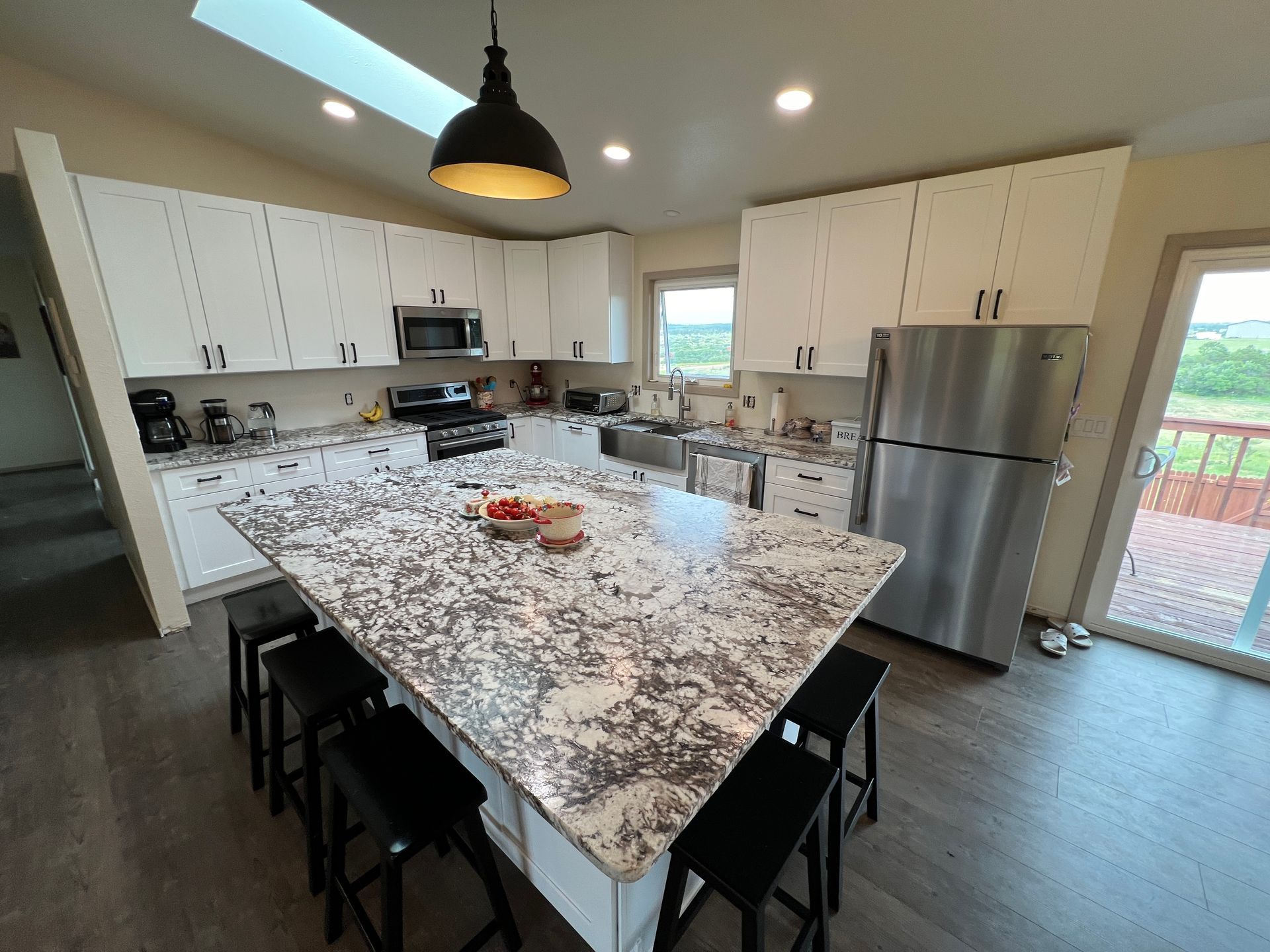 Modern kitchen with white cabinets, granite island with four black stools, stainless steel appliances, and a skylight.