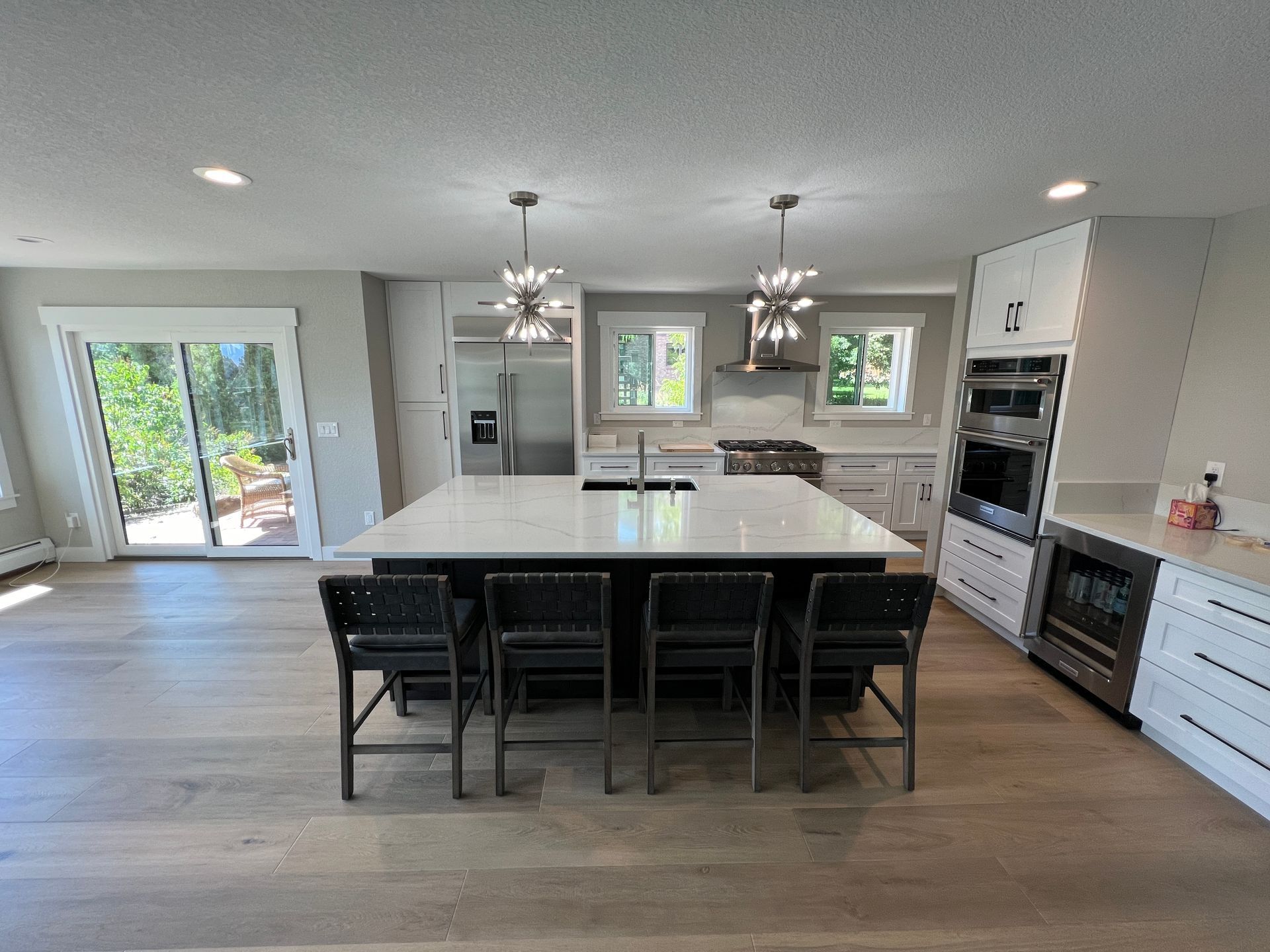 A modern, open-concept kitchen with a large white island, four black bar stools, stainless appliances, and wood flooring.