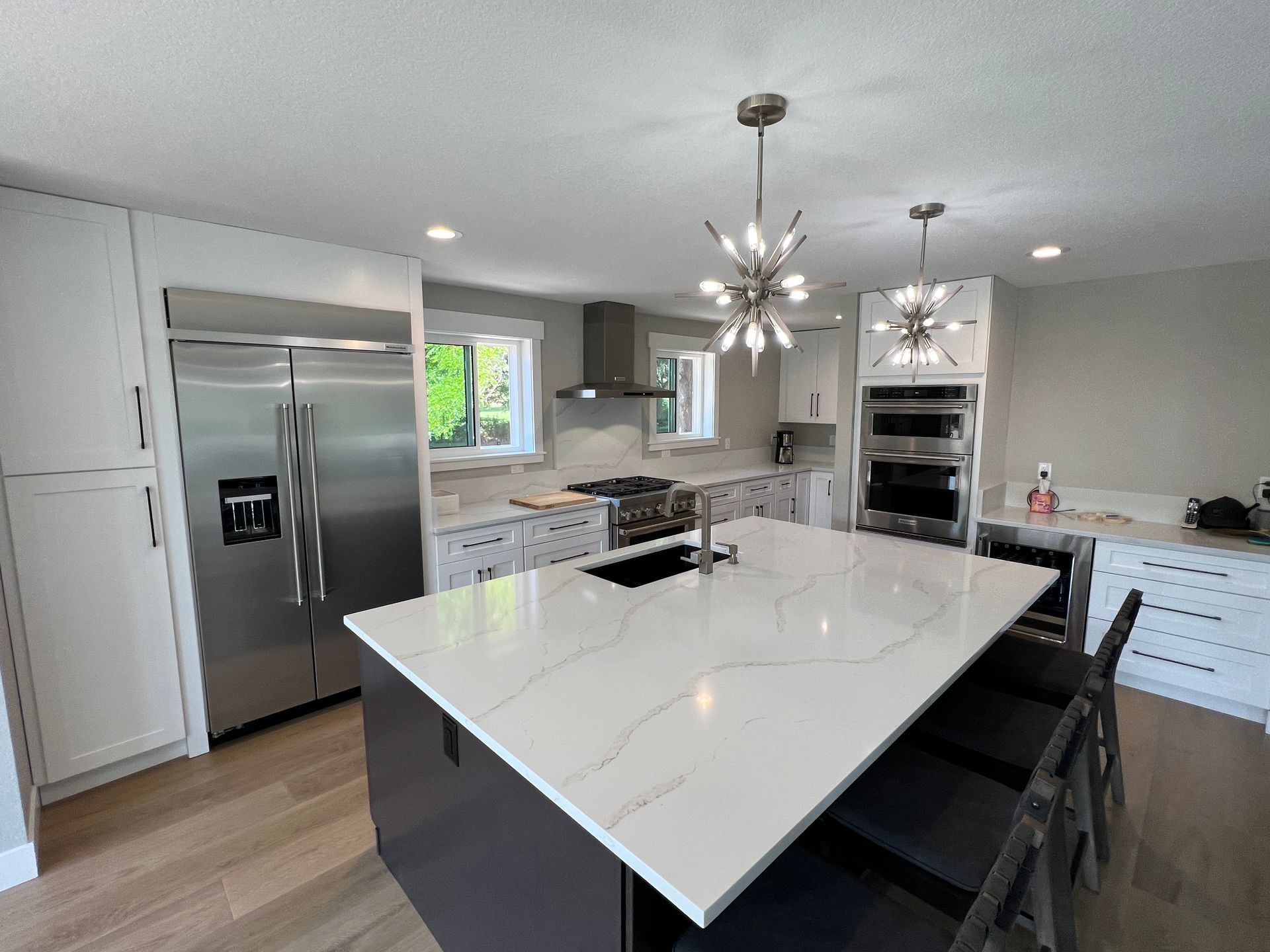 A bright modern kitchen with a white quartz island, dark cabinets, stainless steel appliances, and two star-shaped lights.