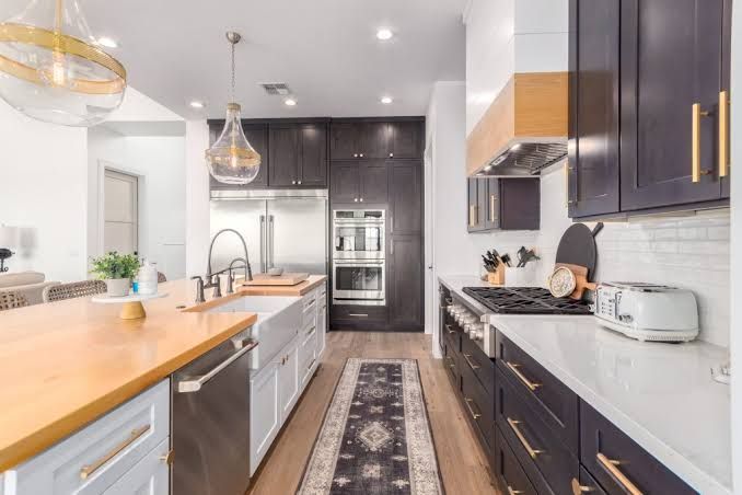 A modern kitchen with dark cabinetry, white countertops, a wood-topped island, and a runner rug on a wood floor.
