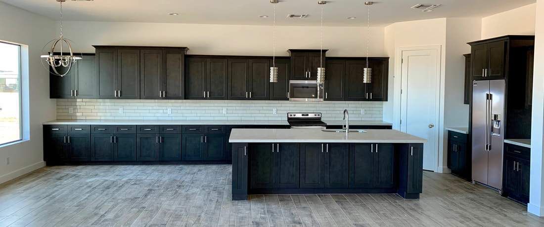 A modern kitchen with dark wood cabinets, a large white-topped island, light wood-look flooring, and stainless appliances.