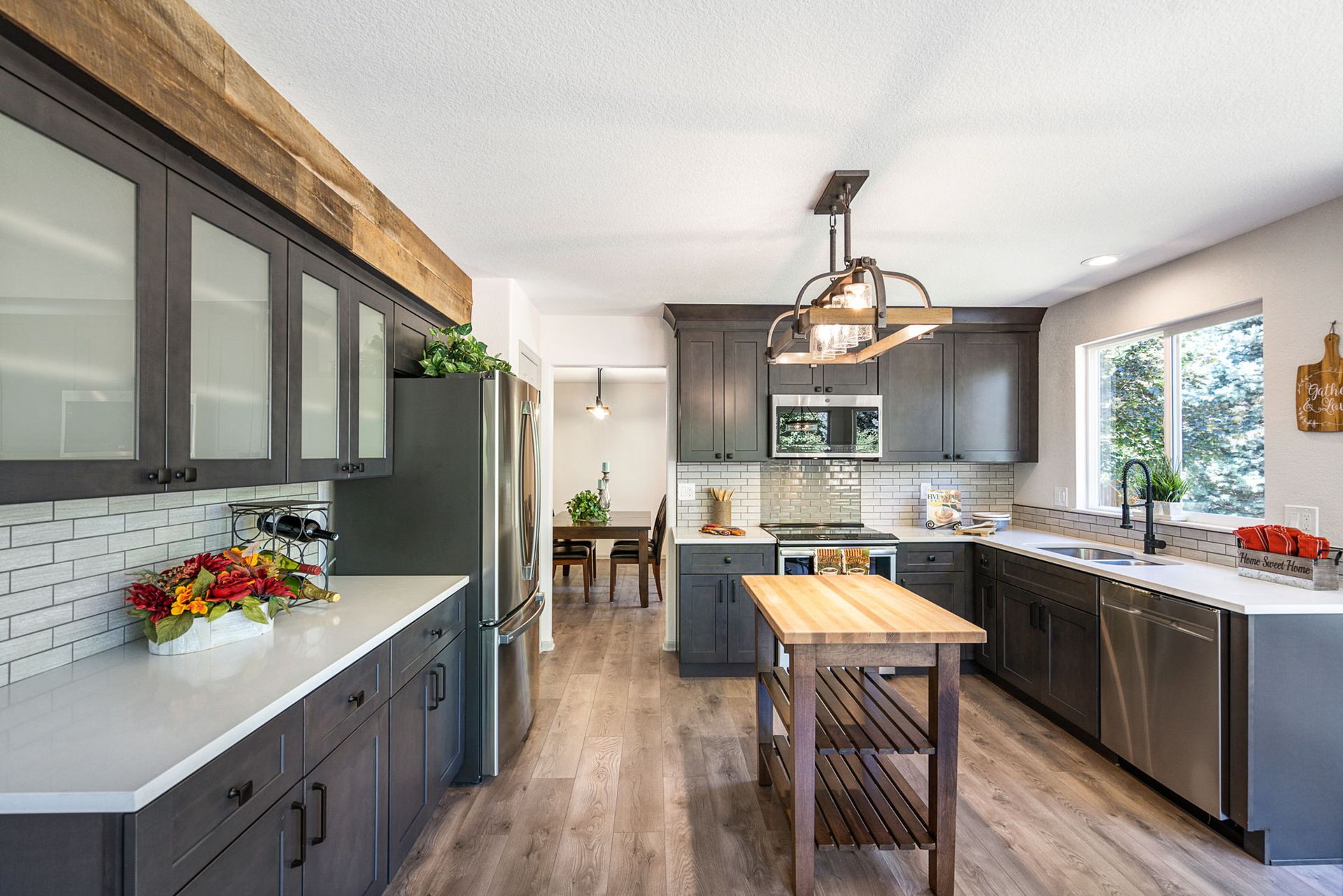 A modern kitchen with dark cabinetry, white countertops, a wooden kitchen island, and a rustic light fixture.