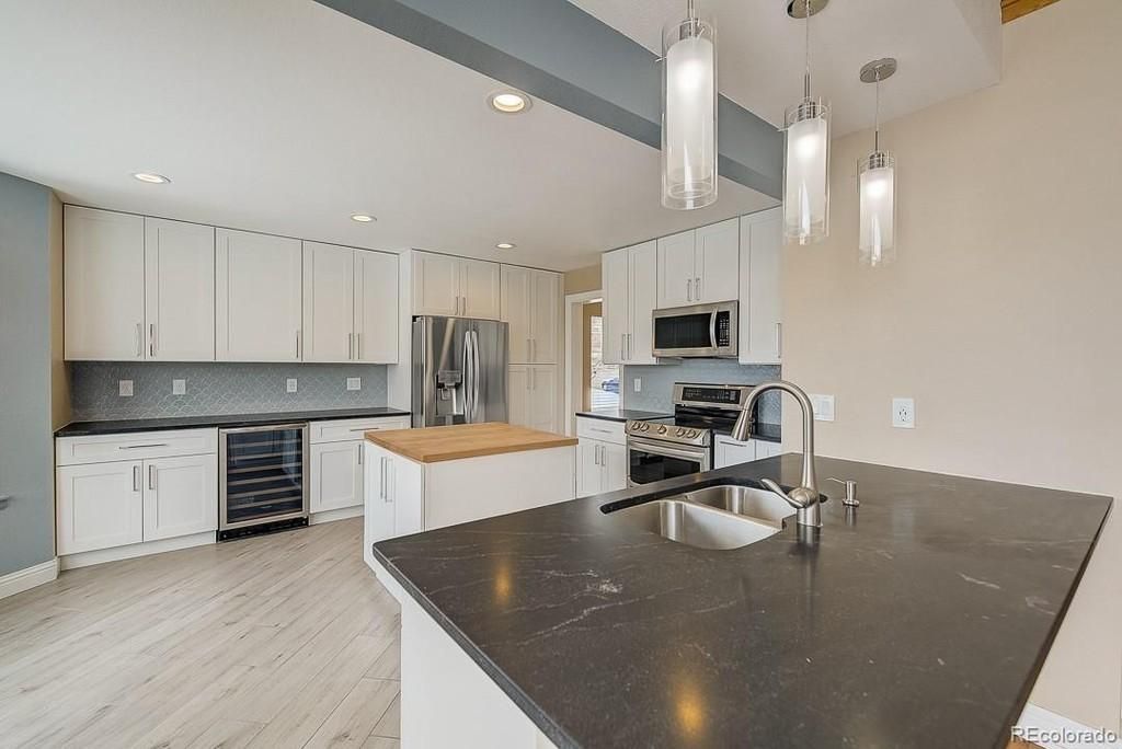 A modern kitchen with white cabinets, dark countertops, a central island, and three pendant lights hanging over the sink.