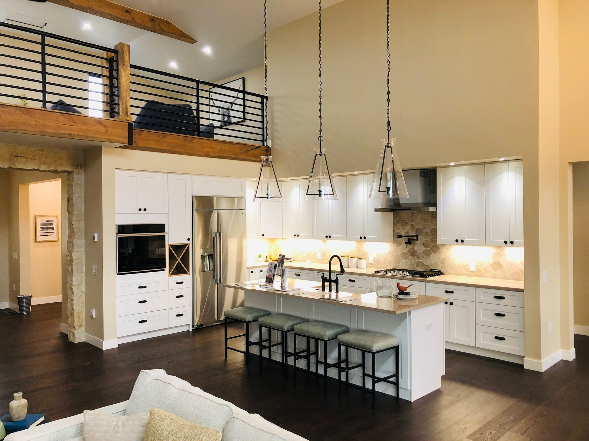 A bright kitchen with white cabinets, a large central island with bar stools, stainless appliances, and a wood loft above.