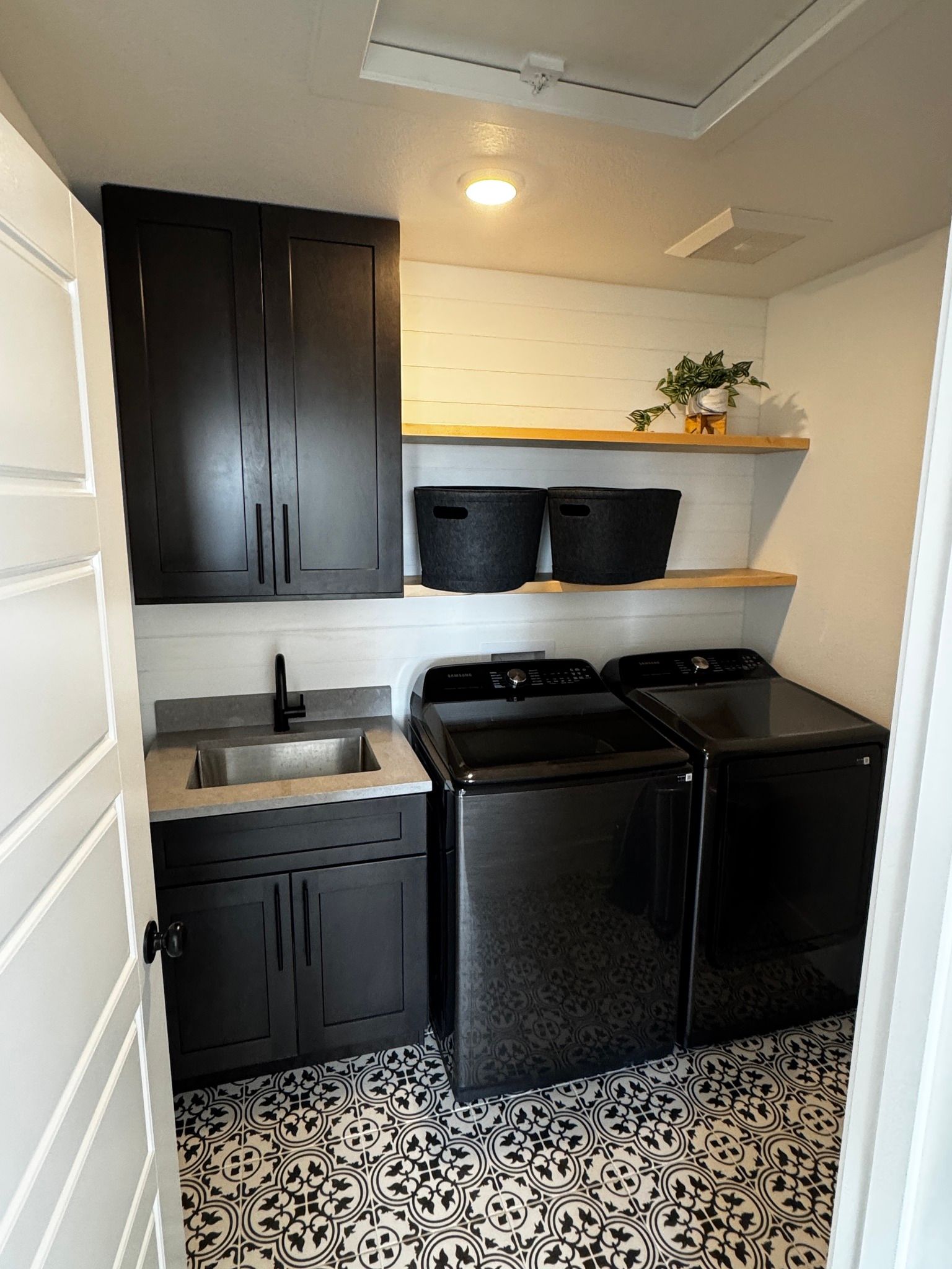 A laundry room with black cabinets, a stainless steel sink, black appliances, and patterned tile flooring.