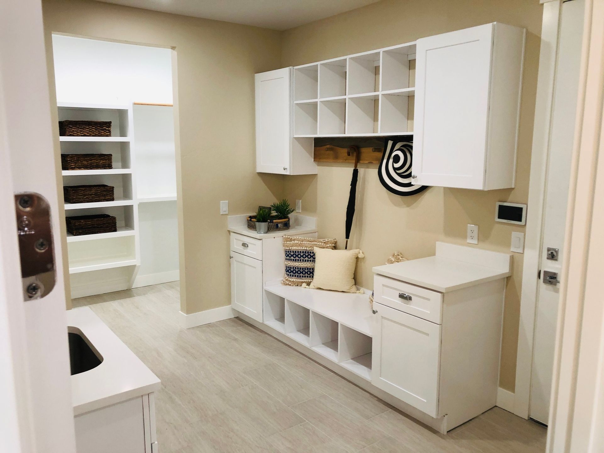 A white mudroom featuring wall-mounted storage, a built-in bench with cubbies, and a view into a walk-in closet.