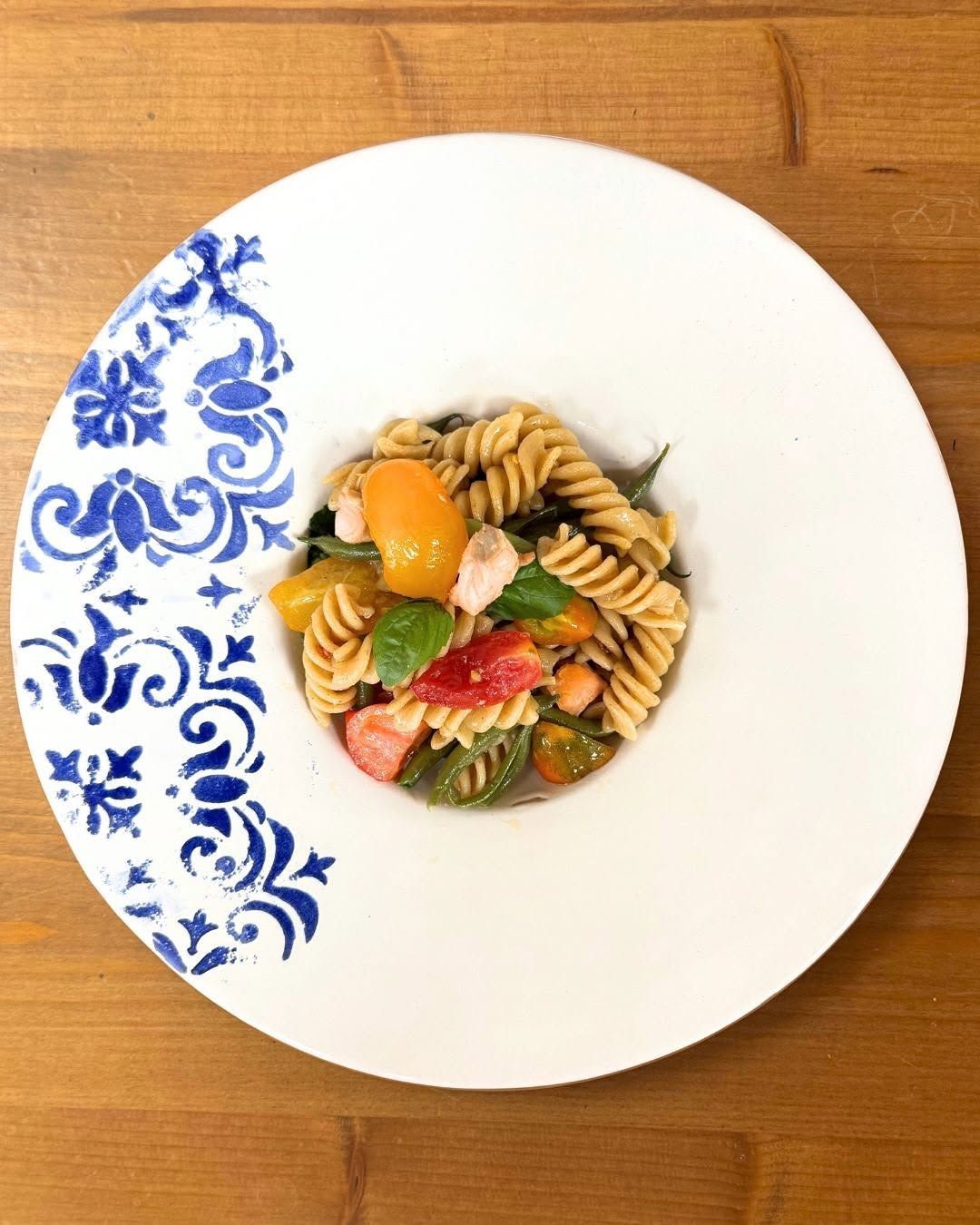 Insalata di pasta in un piatto bianco con bordo floreale blu su un tavolo di legno.