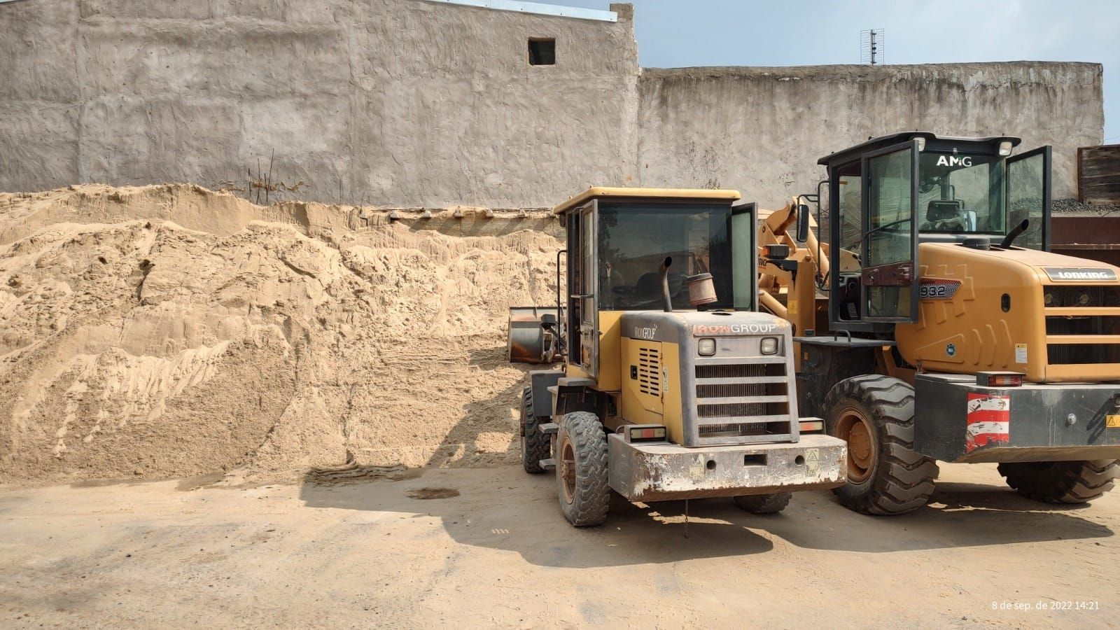 Dos excavadoras están estacionadas una al lado de la otra frente a un montón de arena.