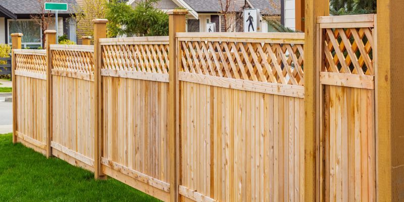 A wooden fence with vertical planks and a diamond-patterned lattice top, bordering a grassy lawn and a suburban street.