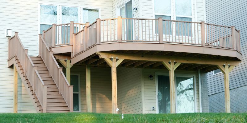 A raised wooden deck with a staircase attached to the back of a light-colored vinyl-sided house.