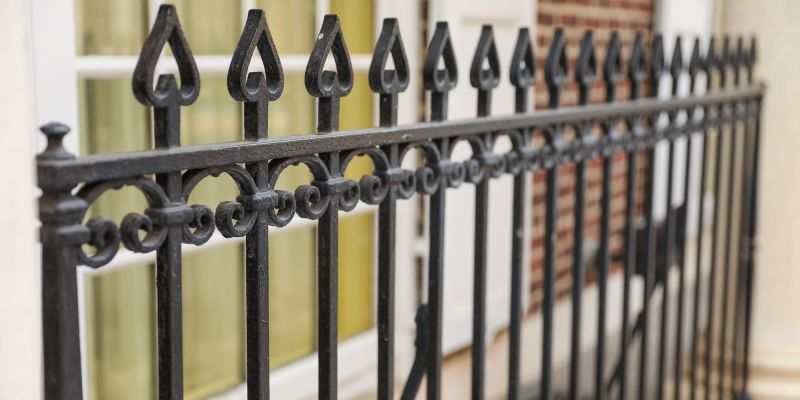 Black decorative wrought iron fence with pointed spade-shaped finials in front of a building.
