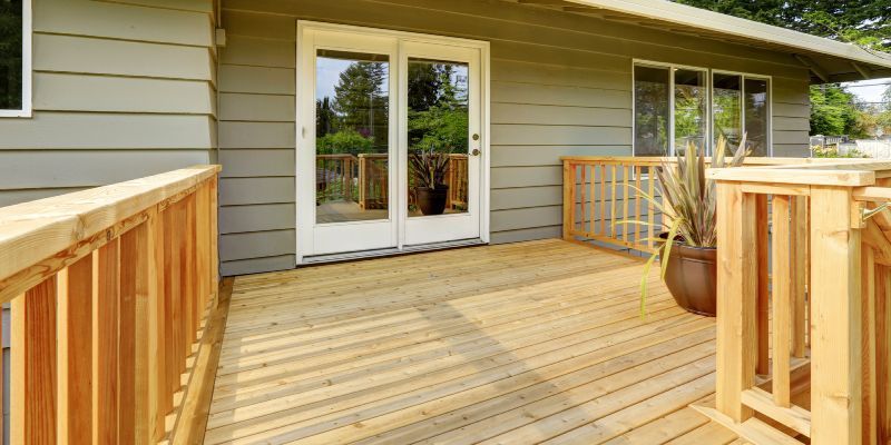A wooden deck with a railing and a plant pot, attached to a house with light-colored horizontal siding and glass doors.