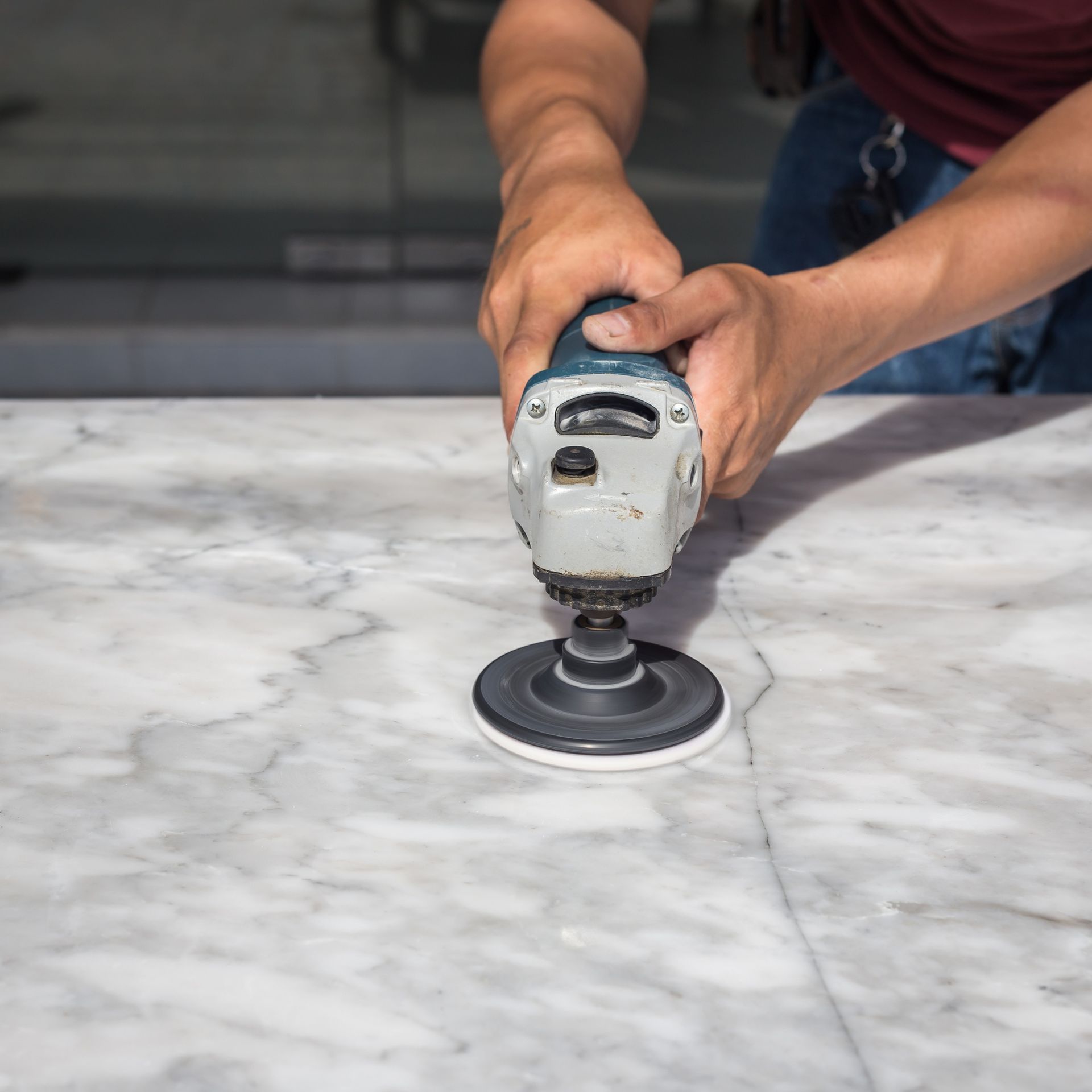 A worker uses a handheld polishing tool to smooth and refine the surface of a white marble countertop.