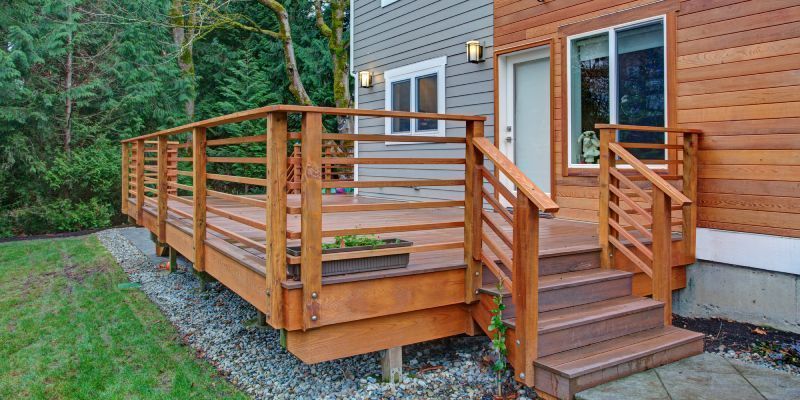 A modern wooden deck with horizontal railings and stairs, attached to a house with gray and wood-paneled siding.