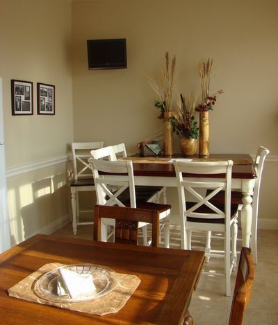 Dining area with a table and four white chairs, a small TV, and decorative vases.