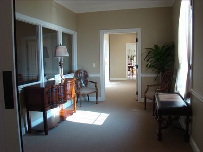 Hallway with beige walls, windows, furniture, and a potted plant.